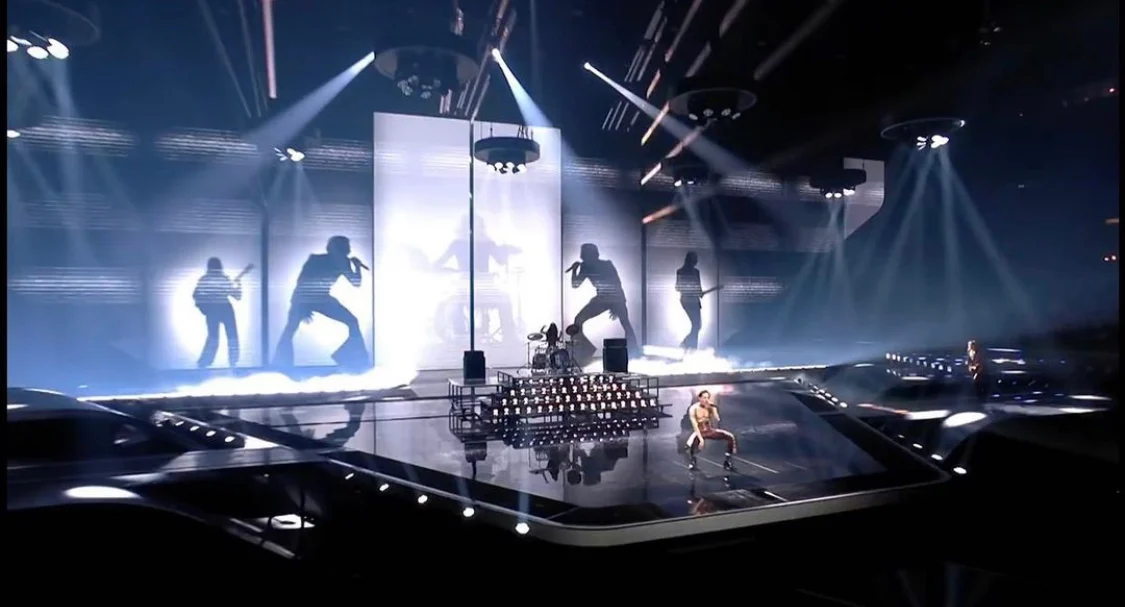 Wide view of the Eurovision 2021 stage: giant band silhouettes on white backdrops, light beams and a mirrored floor – Måneskin at Eurovision 2021, Rotterdam, Netherlands – concert stage design