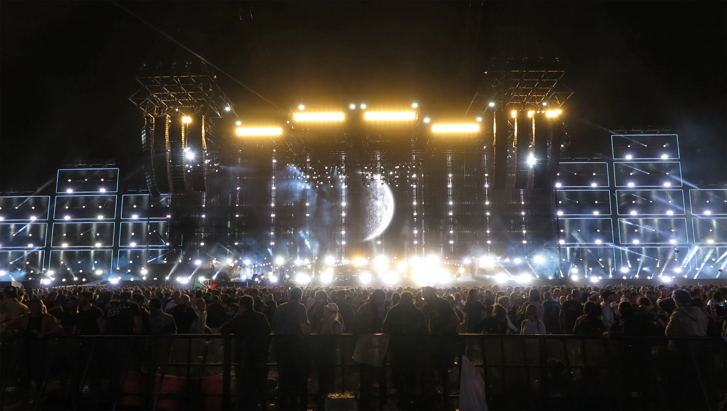 Night view of the full stage with golden light bars, screen-covered side towers and a moon image at centre – Vasco Rossi Modena Park, Italy, 2017 – concert stage design