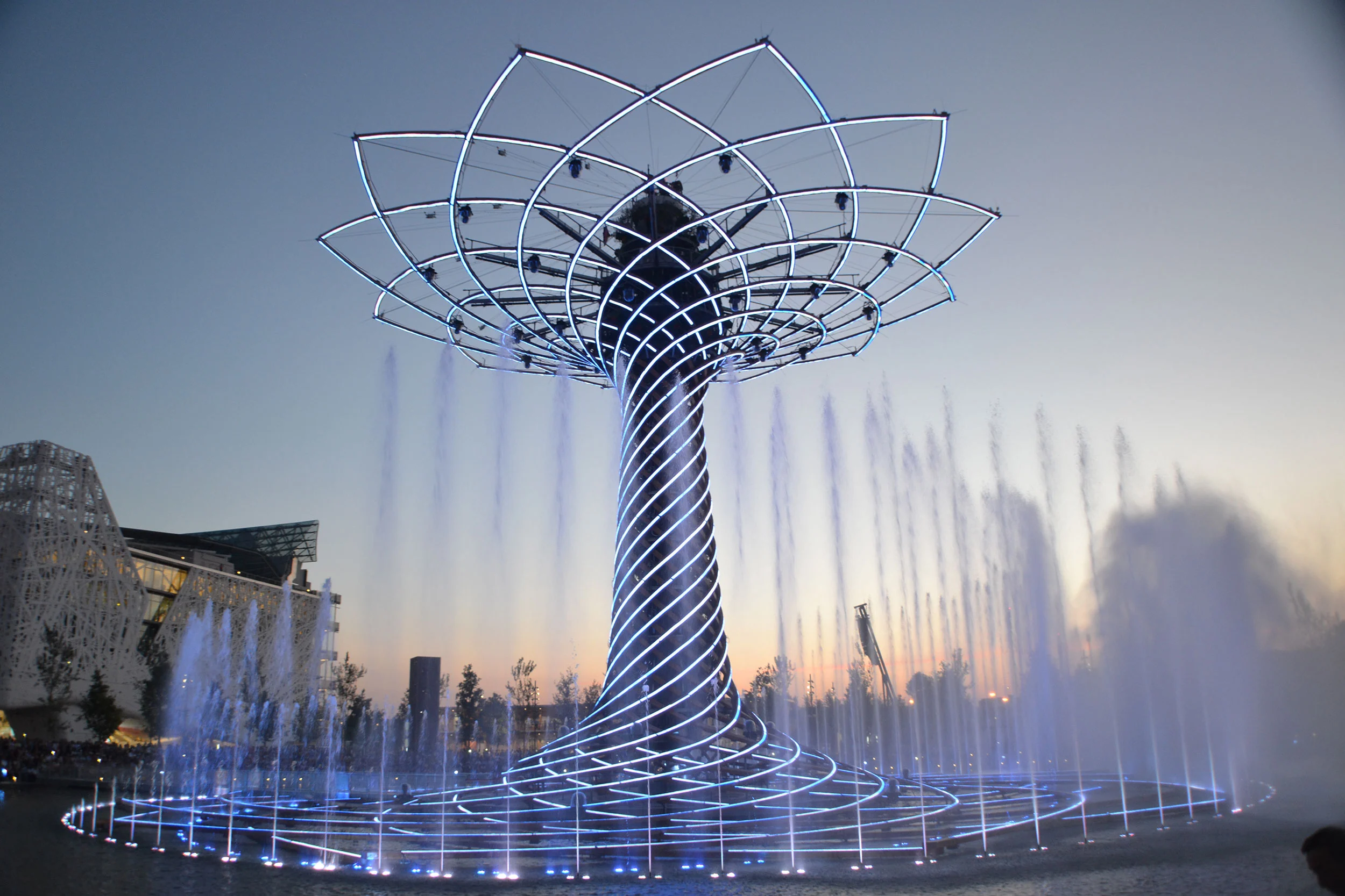 Tree of Life at dusk: steel lattice crown and spiralling trunk rising above a ring of water jets – Albero della Vita at Expo 2015, Milan, Italy – installation design