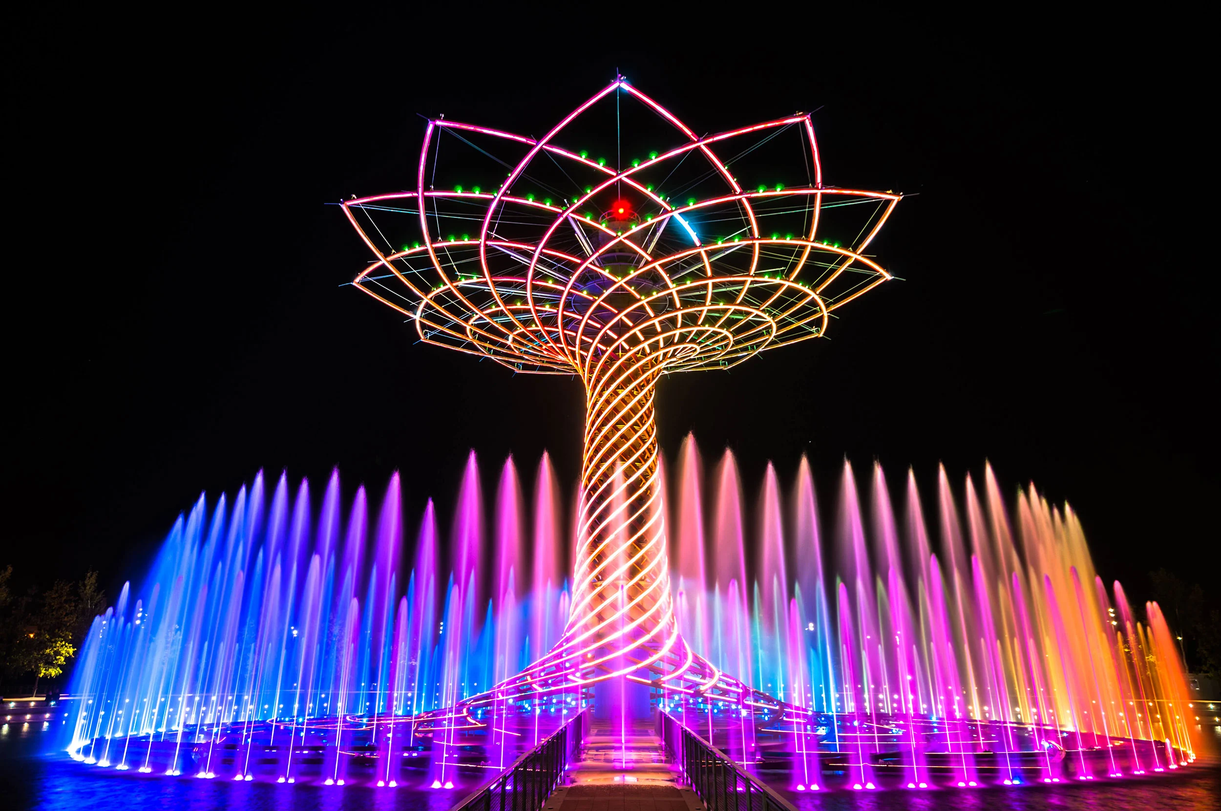 Tree of Life glowing in pink, orange and violet, with multicoloured fountain jets around it – Albero della Vita at Expo 2015, Milan, Italy – installation design