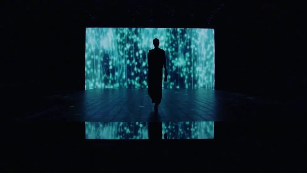 Silhouette of a model walking toward an LED wall of teal light streaks, reflected on the floor – Giorgio Armani SS21 Womenswear, Milan, Italy, 2021 – fashion show set design
