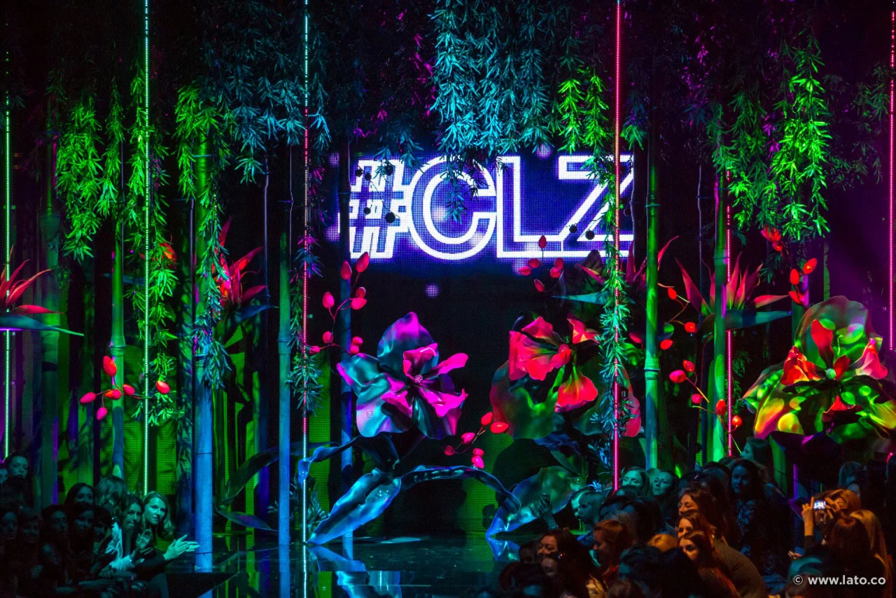 Set detail of the #CLZ neon sign among hanging greenery, oversized flowers and neon tubes – Calzedonia SS15 Collection, Italy, 2015 – fashion show set design