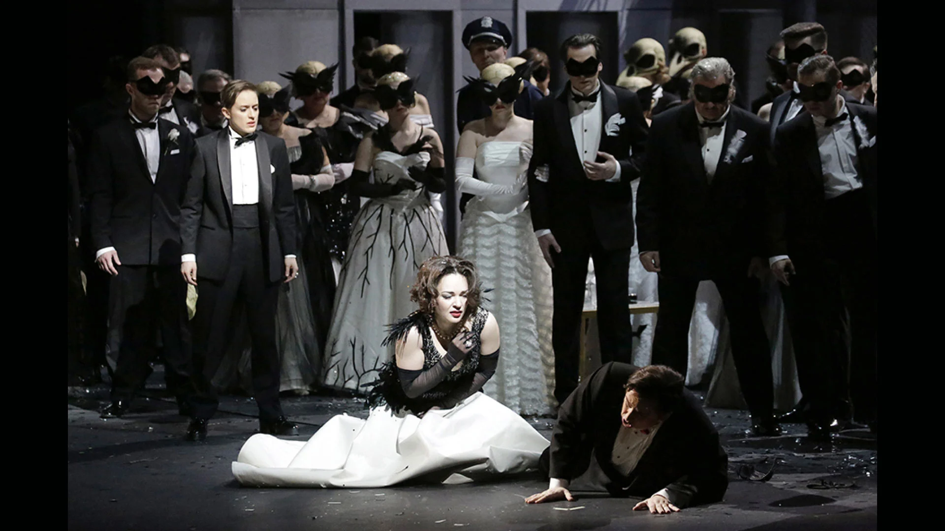 Woman in a white gown kneeling beside a fallen man, surrounded by masked guests in evening dress – Un Ballo in Maschera at the Bolshoi Theatre, Moscow, Russia, 2018 – opera set design