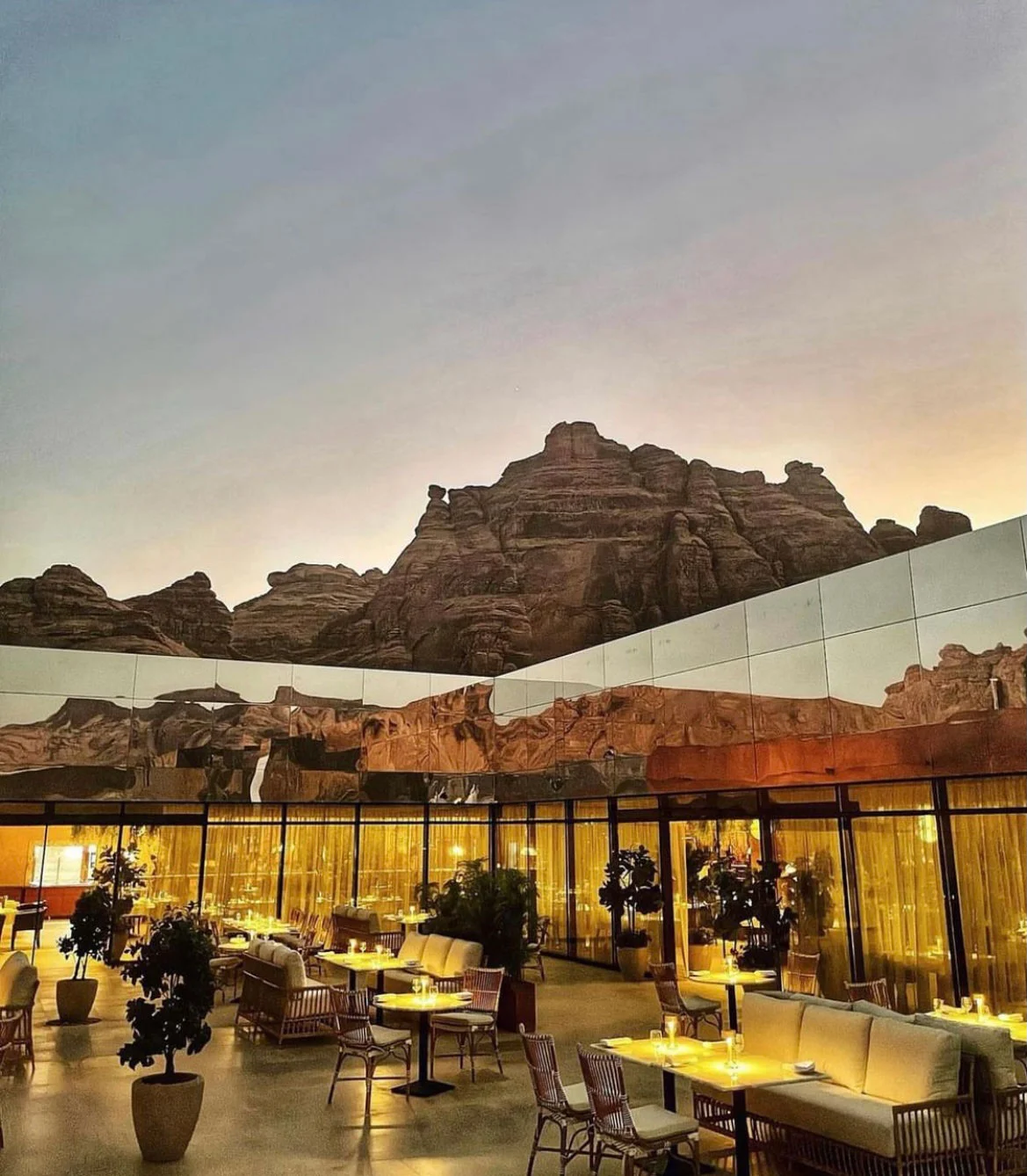 Restaurant terrace at dusk with lit tables and rattan chairs, cliffs reflected in the mirrored wall above – Maraya Concert Hall, AlUla, Saudi Arabia, 2019 – architecture