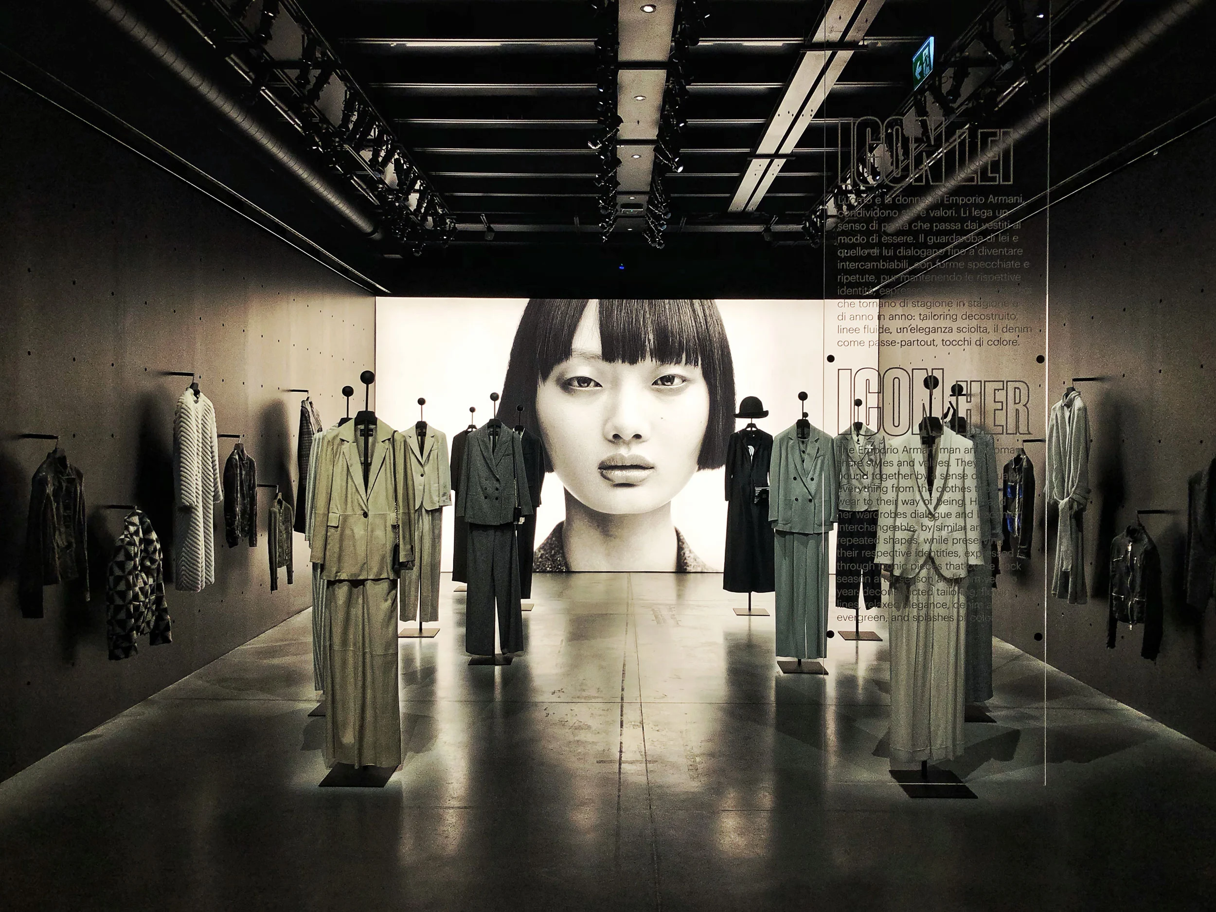 Room of suits on stands leading to a large black-and-white portrait, with text on a glass panel – Emporio Armani The Way We Are, Milan, Italy, 2020 – exhibition design