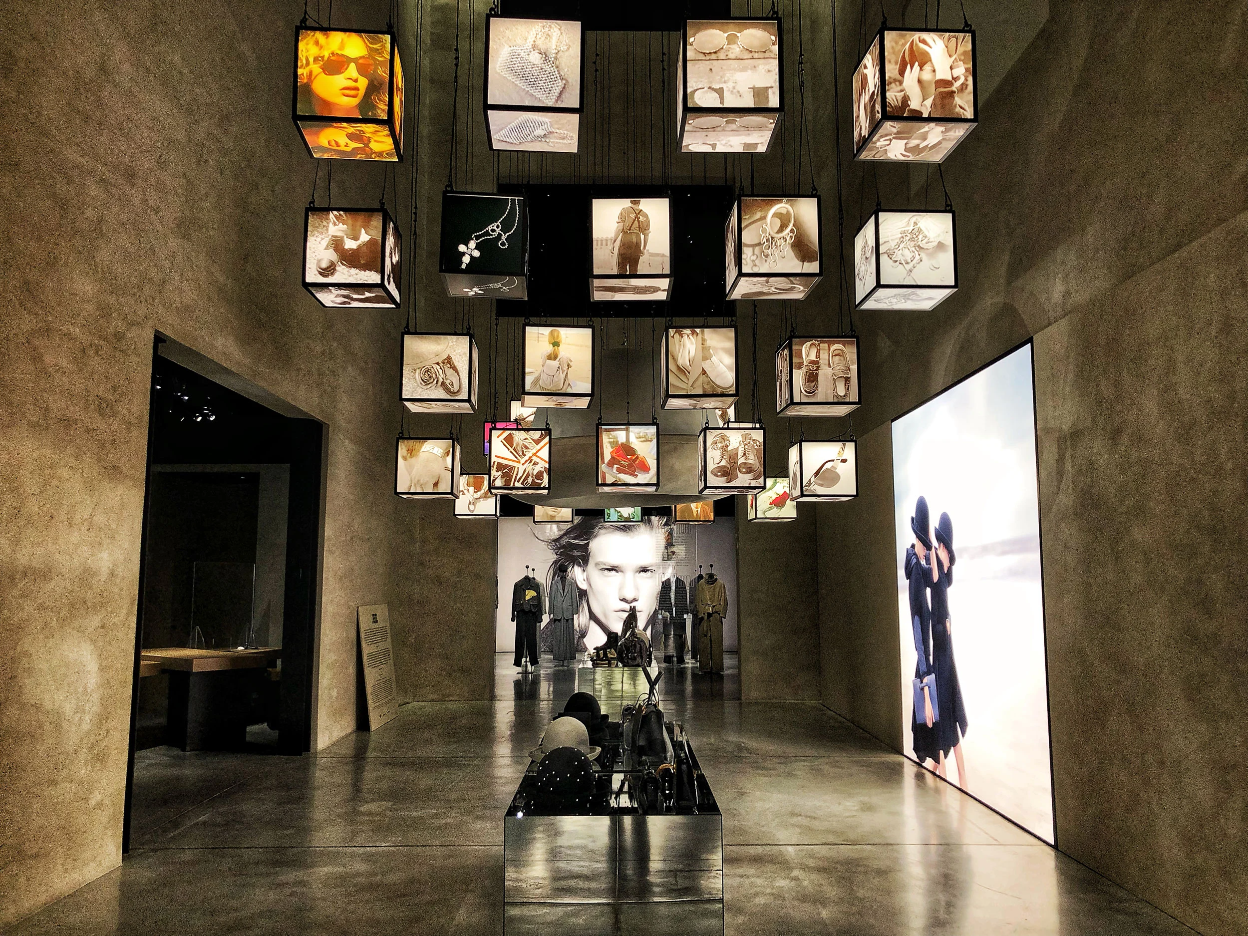 Exhibition hall with illuminated cubes of accessory images hanging from the ceiling, a lightbox at right – Emporio Armani The Way We Are, Milan, Italy, 2020 – exhibition design