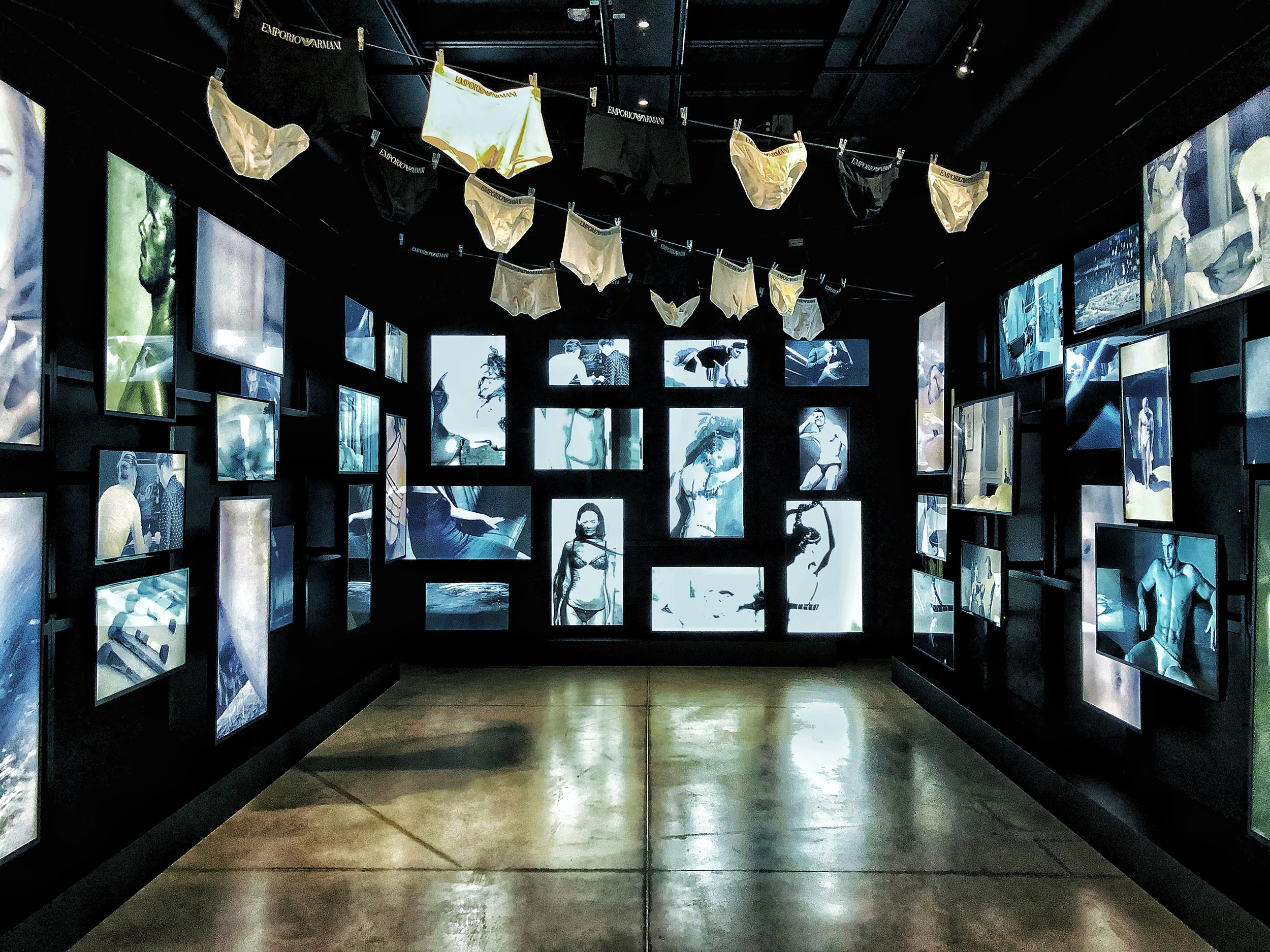 Dark room of backlit underwear advertising images, with briefs hung on a line overhead – Emporio Armani The Way We Are, Milan, Italy, 2020 – exhibition design