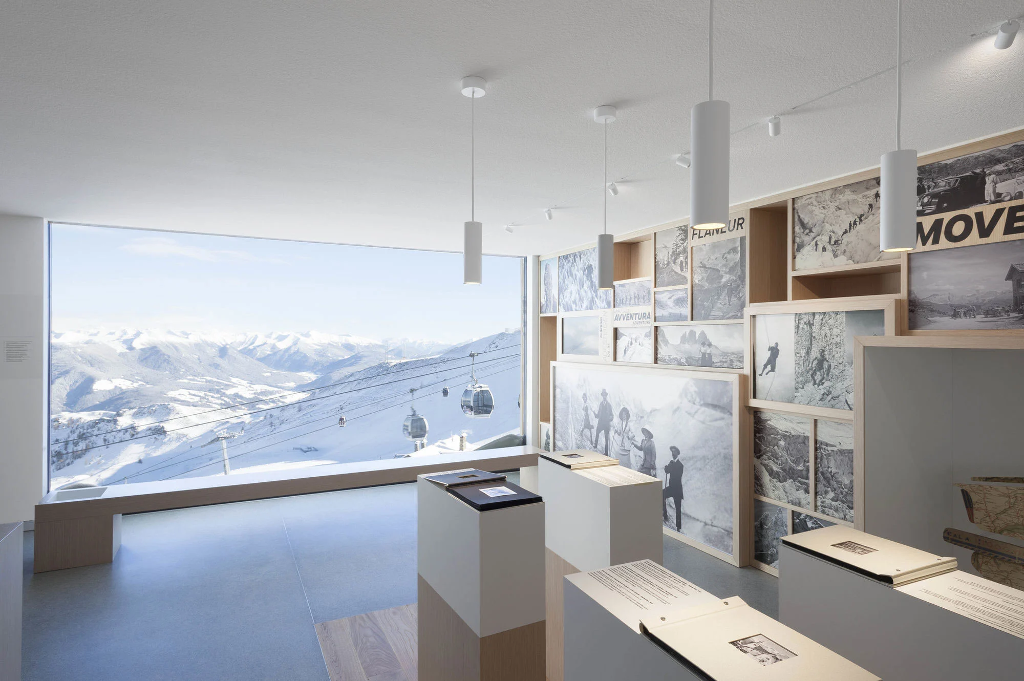 Exhibition room of historic mountain photographs and display stands beside a panoramic window over ski slopes and cable cars – Lumen Museum of Mountain Photography, Kronplatz, Italy, 2018 – architecture
