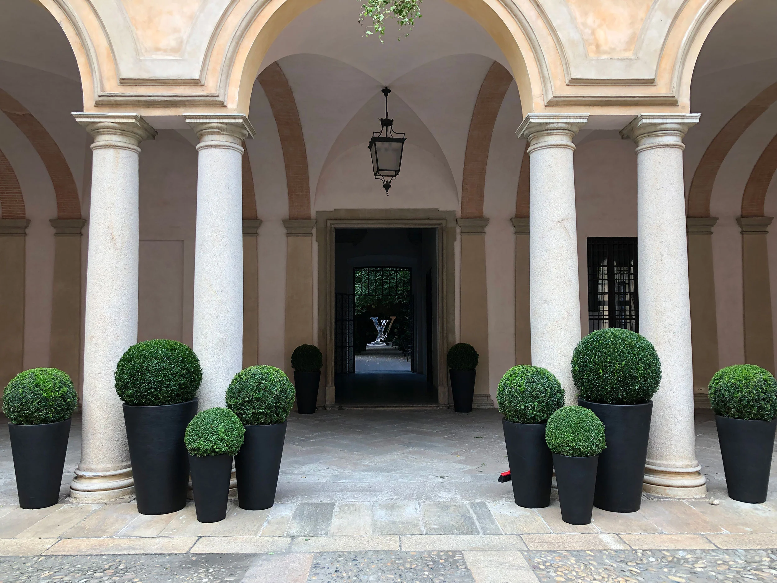 Colonnade with granite columns and black pots of topiary balls framing a doorway to the garden – Louis Vuitton at Palazzo Clerici, Milan, Italy, 2019 – exhibition design