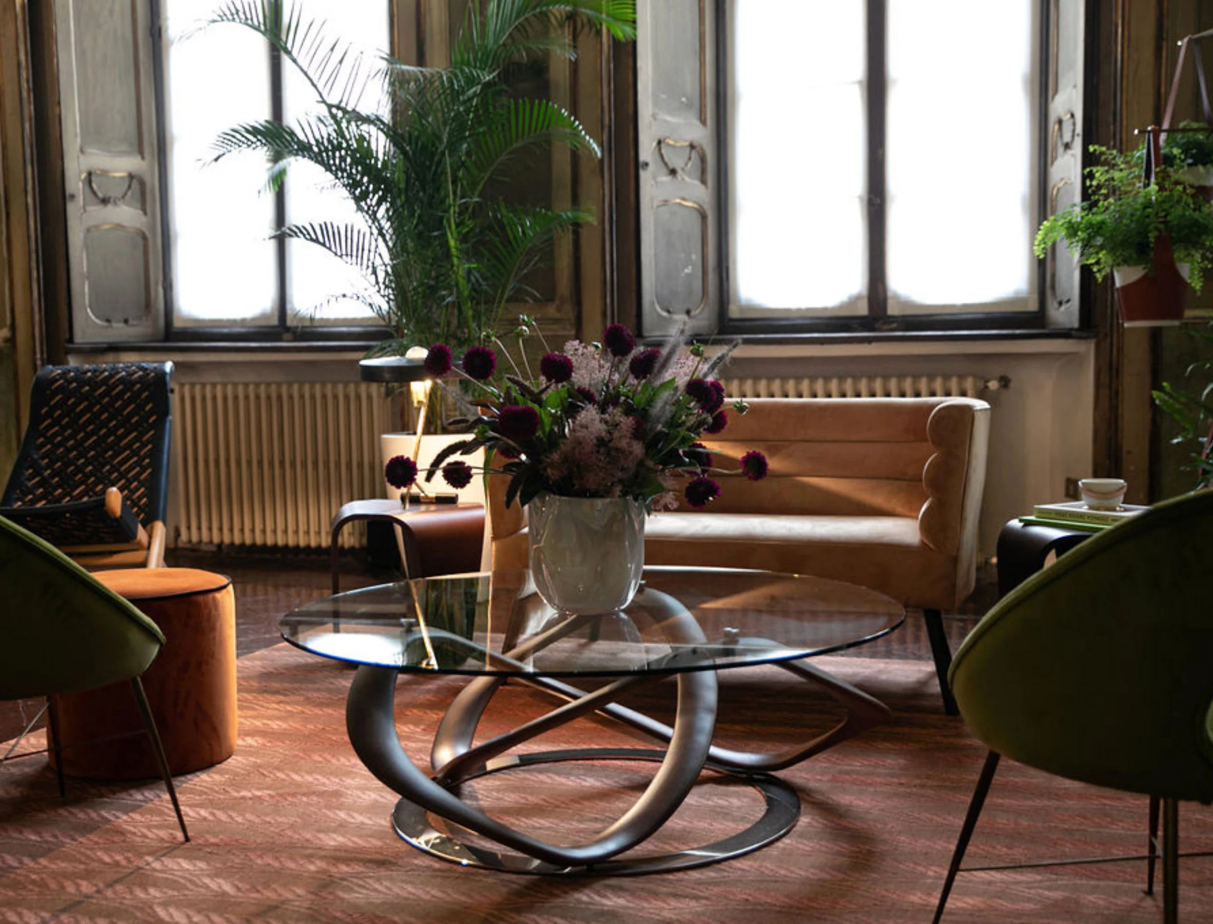 Corner by tall windows with a glass sculptural table, purple flowers and an amber velvet sofa – Louis Vuitton at Palazzo Clerici, Milan, Italy, 2019 – exhibition design