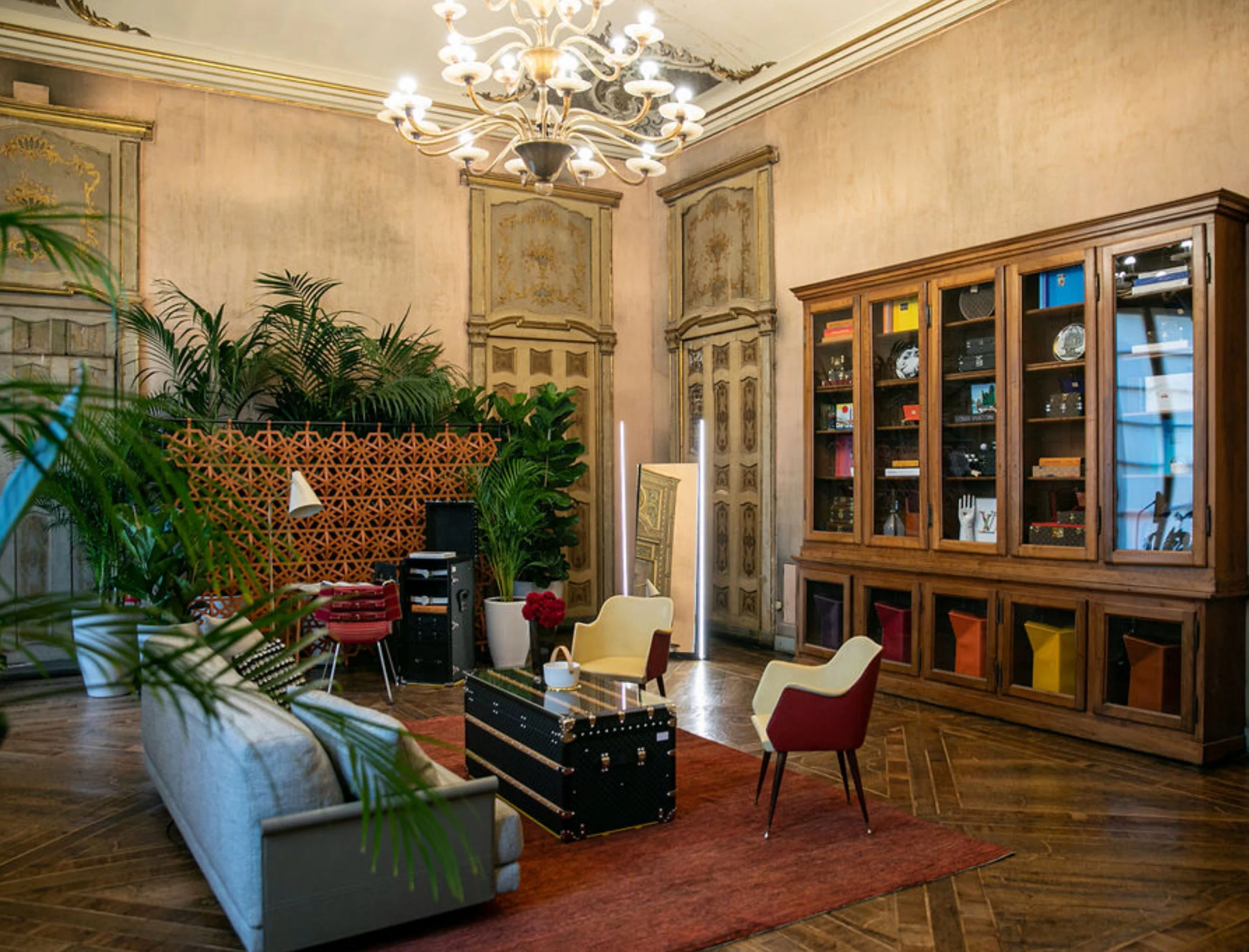 Salon with a crystal chandelier, a trunk used as coffee table and a wooden bookcase of objects – Louis Vuitton at Palazzo Clerici, Milan, Italy, 2019 – exhibition design