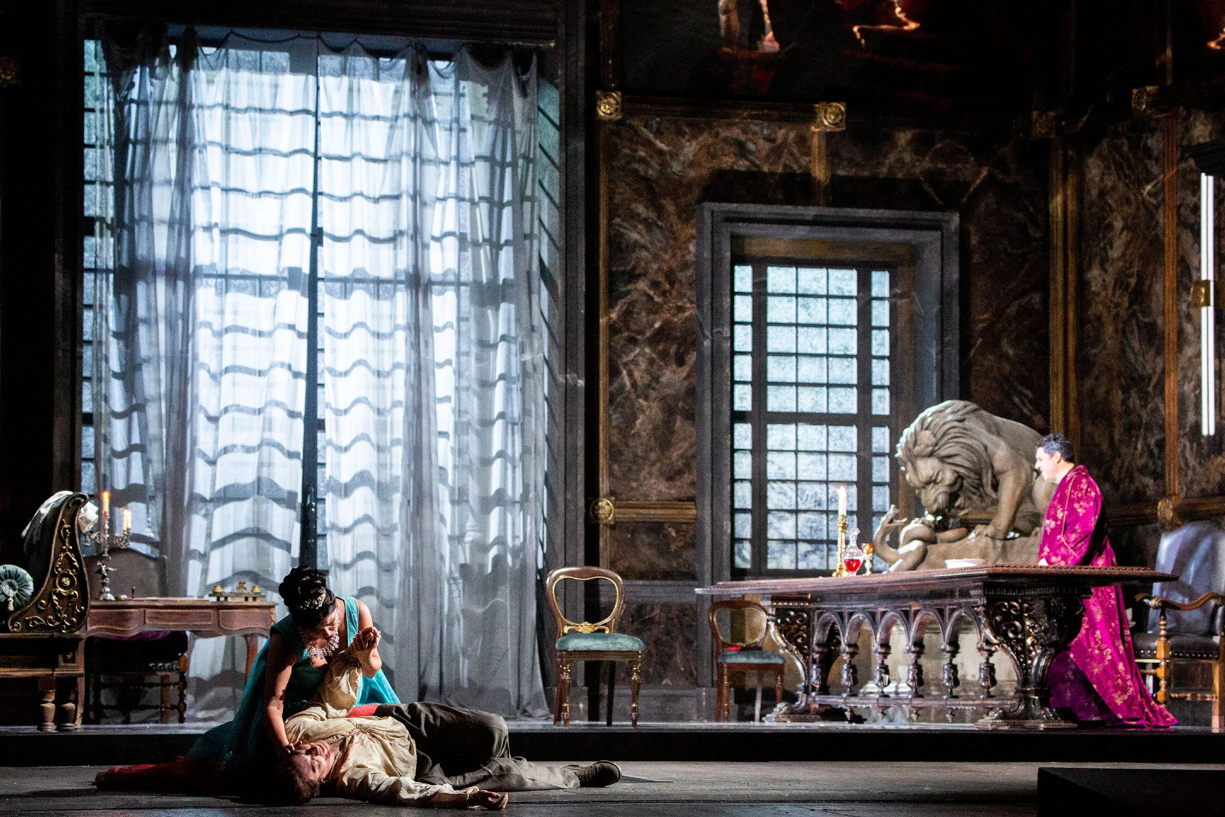 Tosca in Scarpia's palace: a woman bent over a fallen man, a lion sculpture and tall curtained window – Tosca at La Scala, Milan, Italy, 2019 – opera set design