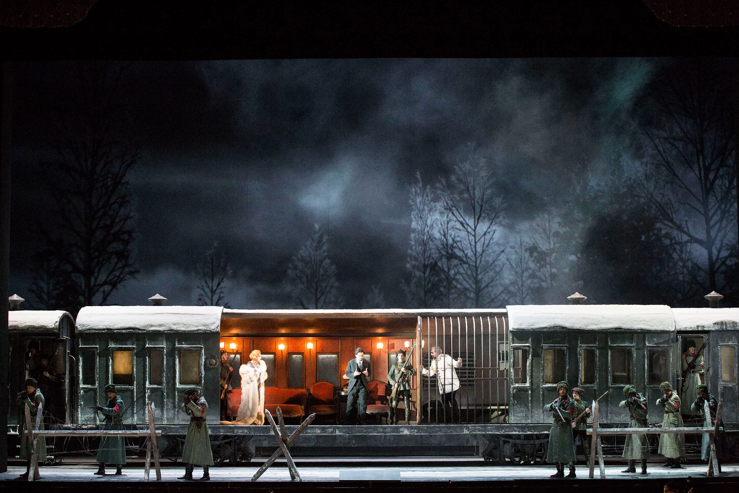 Railway carriage set in a snowy forest at night, a lit saloon car with performers and soldiers in front – Tamerlano at La Scala, Milan, Italy, 2017 – opera set design
