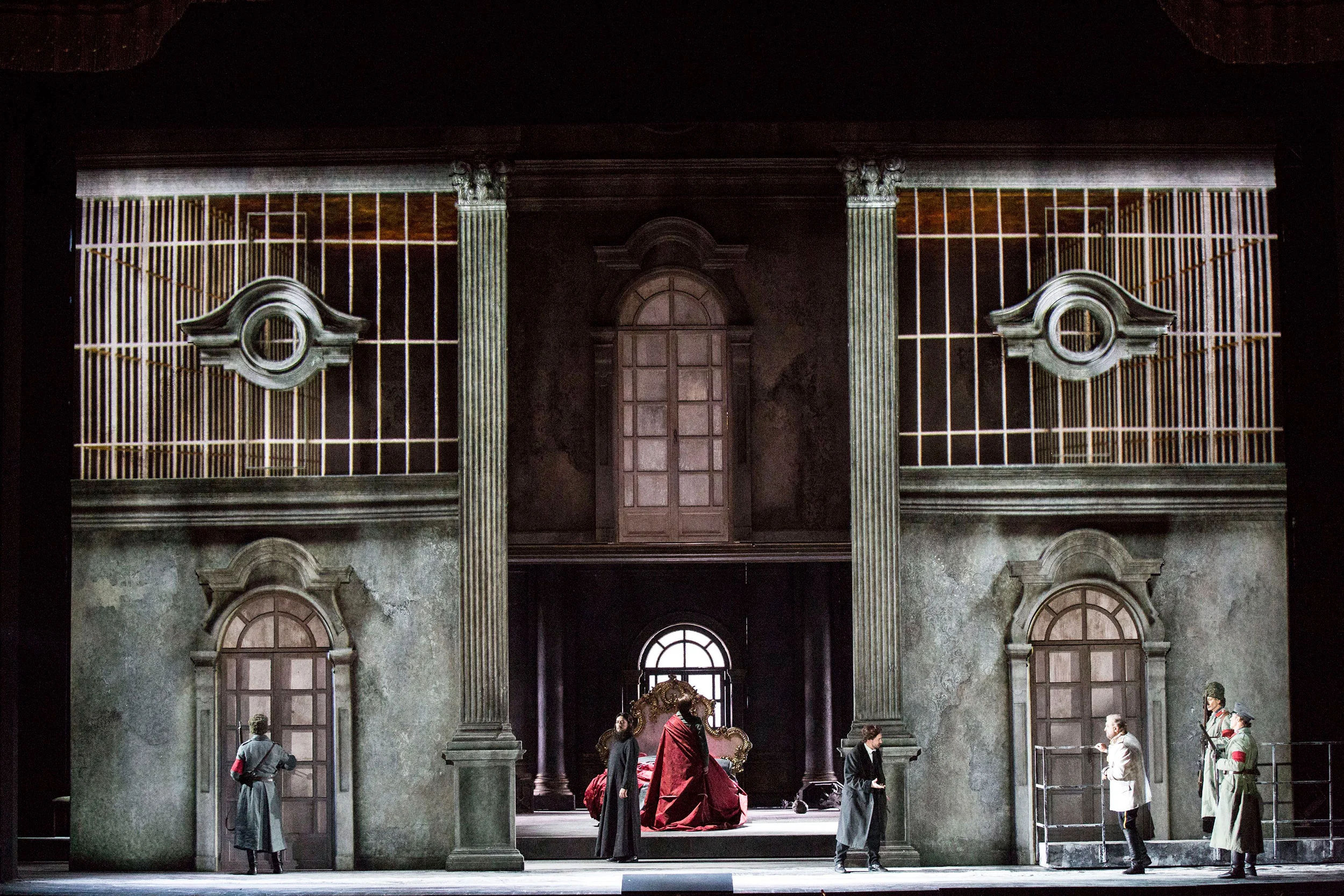 Tamerlano set: weathered palace facade with arched windows and grilles, a figure in red on a throne at centre – Tamerlano at La Scala, Milan, Italy, 2017 – opera set design