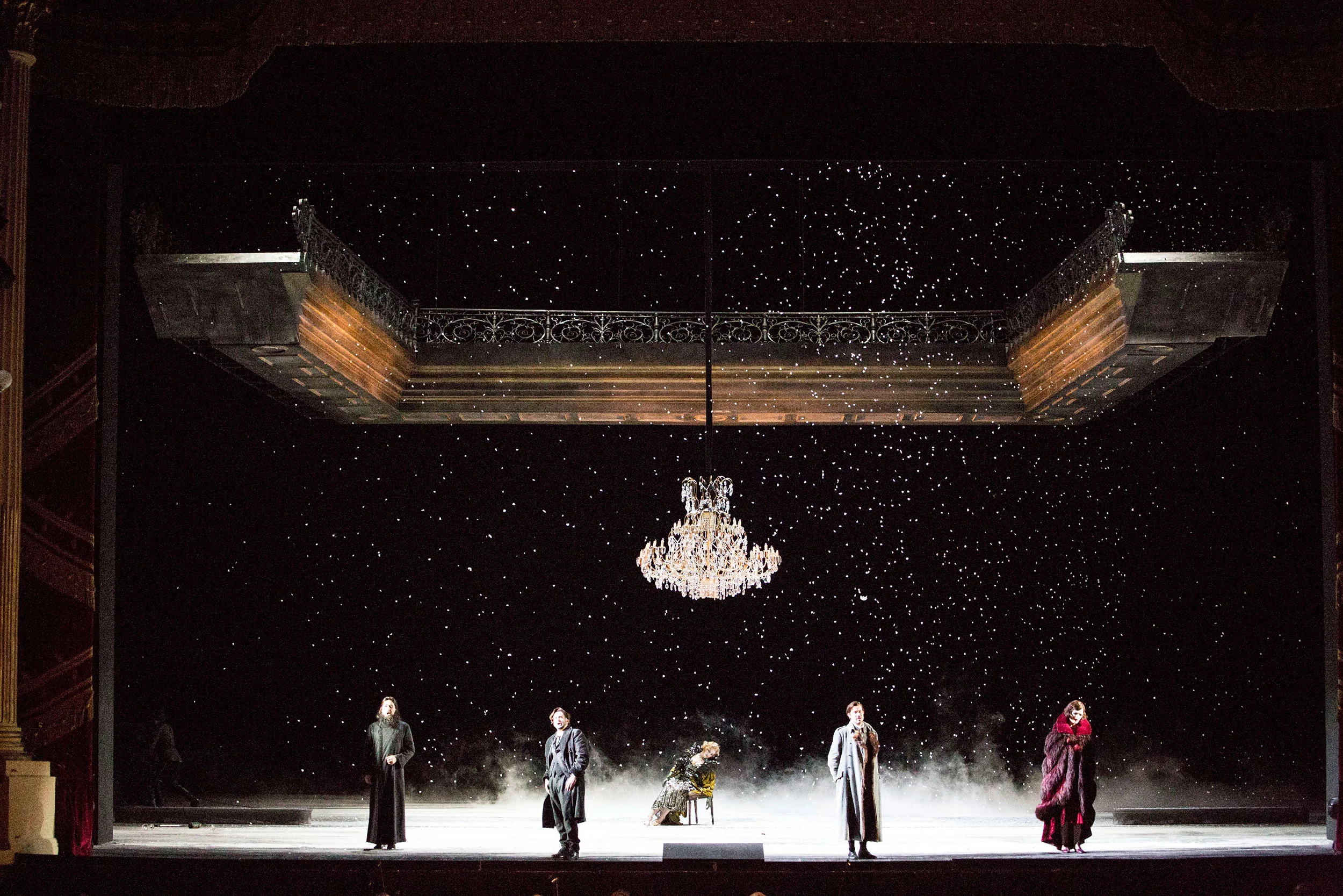 Snow falling on a dark stage with a crystal chandelier and a suspended balcony above five performers – Tamerlano at La Scala, Milan, Italy, 2017 – opera set design
