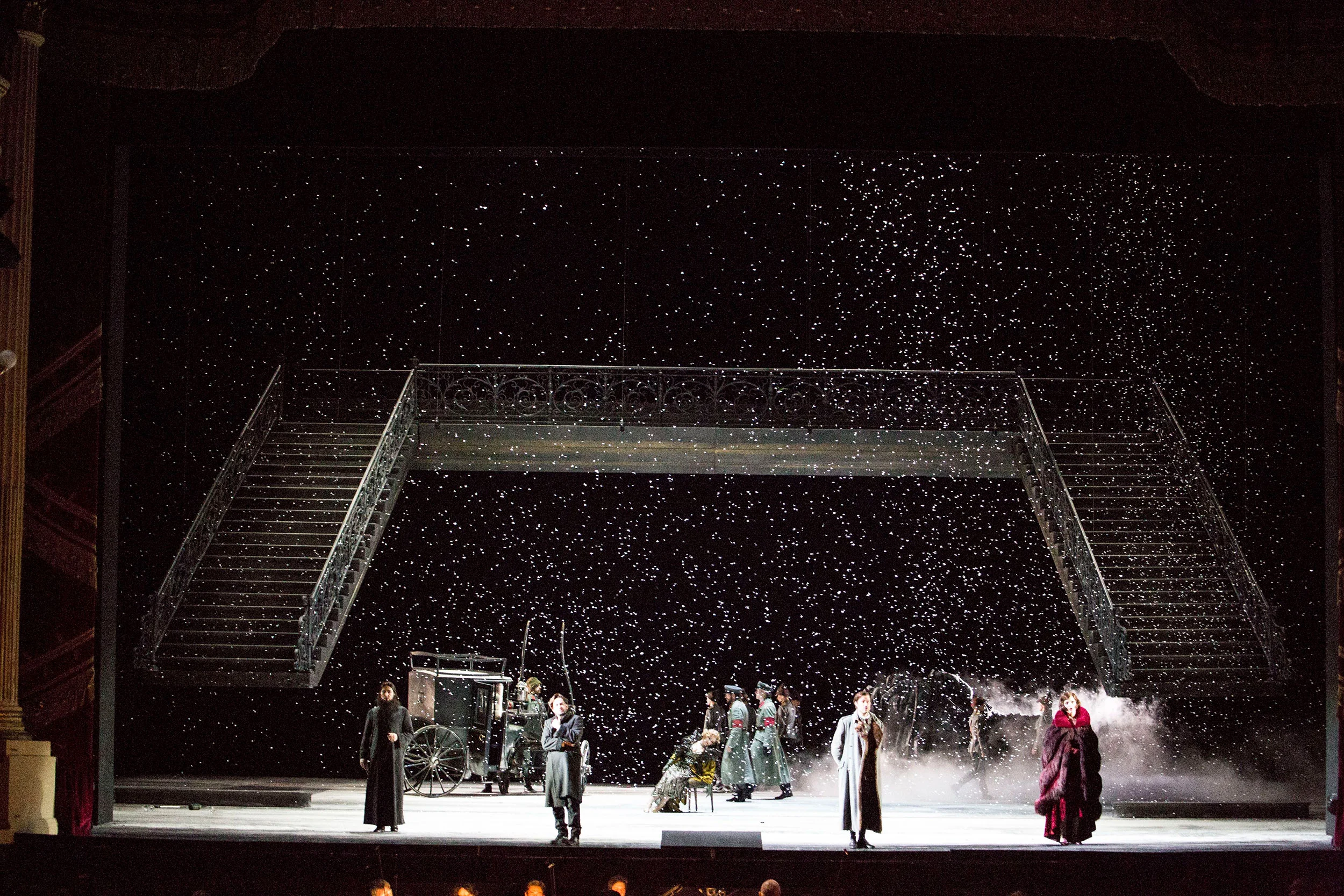 Wide view of the snowy scene: double staircase and bridge, carriage and performers spread across the stage – Tamerlano at La Scala, Milan, Italy, 2017 – opera set design