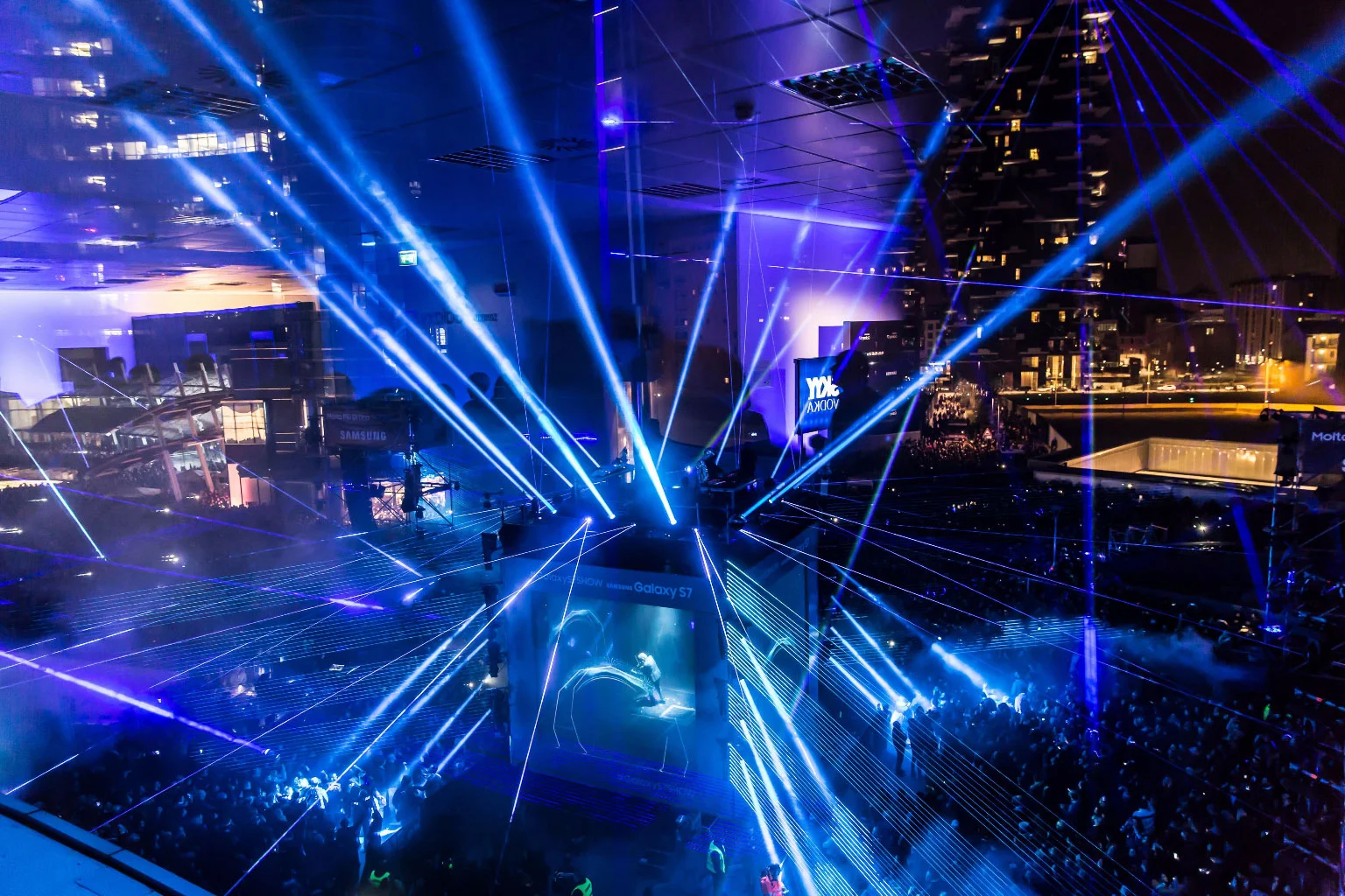 Aerial view of the Samsung Galaxy S7 laser show: blue laser beams criss-crossing over the crowd and stage – Samsung Galaxy S7 Laser Show, Milan, Italy, 2016 – event design