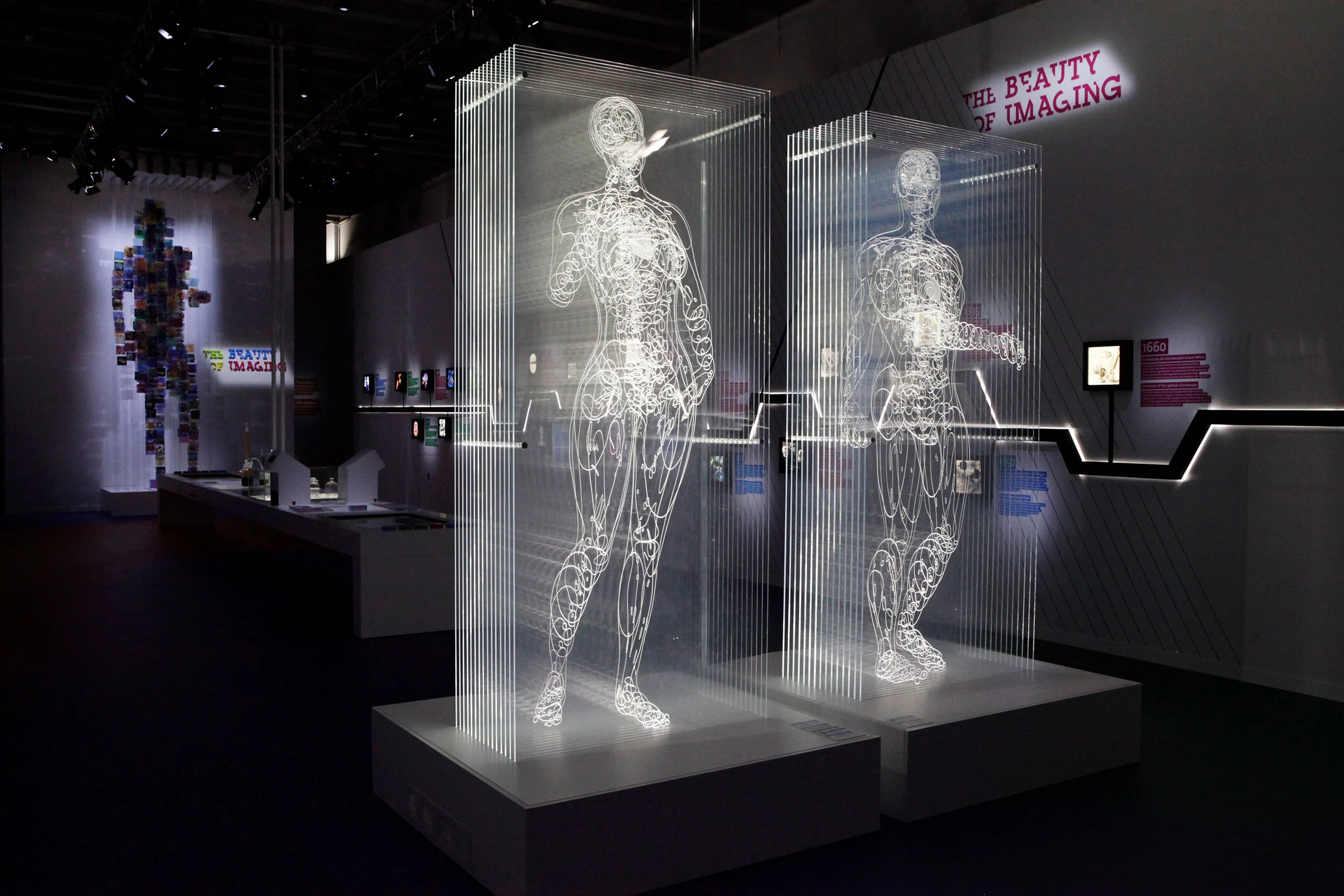 Two transparent human figures etched in light on vertical layers, in the dark The Beauty of Imaging exhibition – Bracco The Beauty of Imaging, Milan, Italy, 2017 – exhibition design