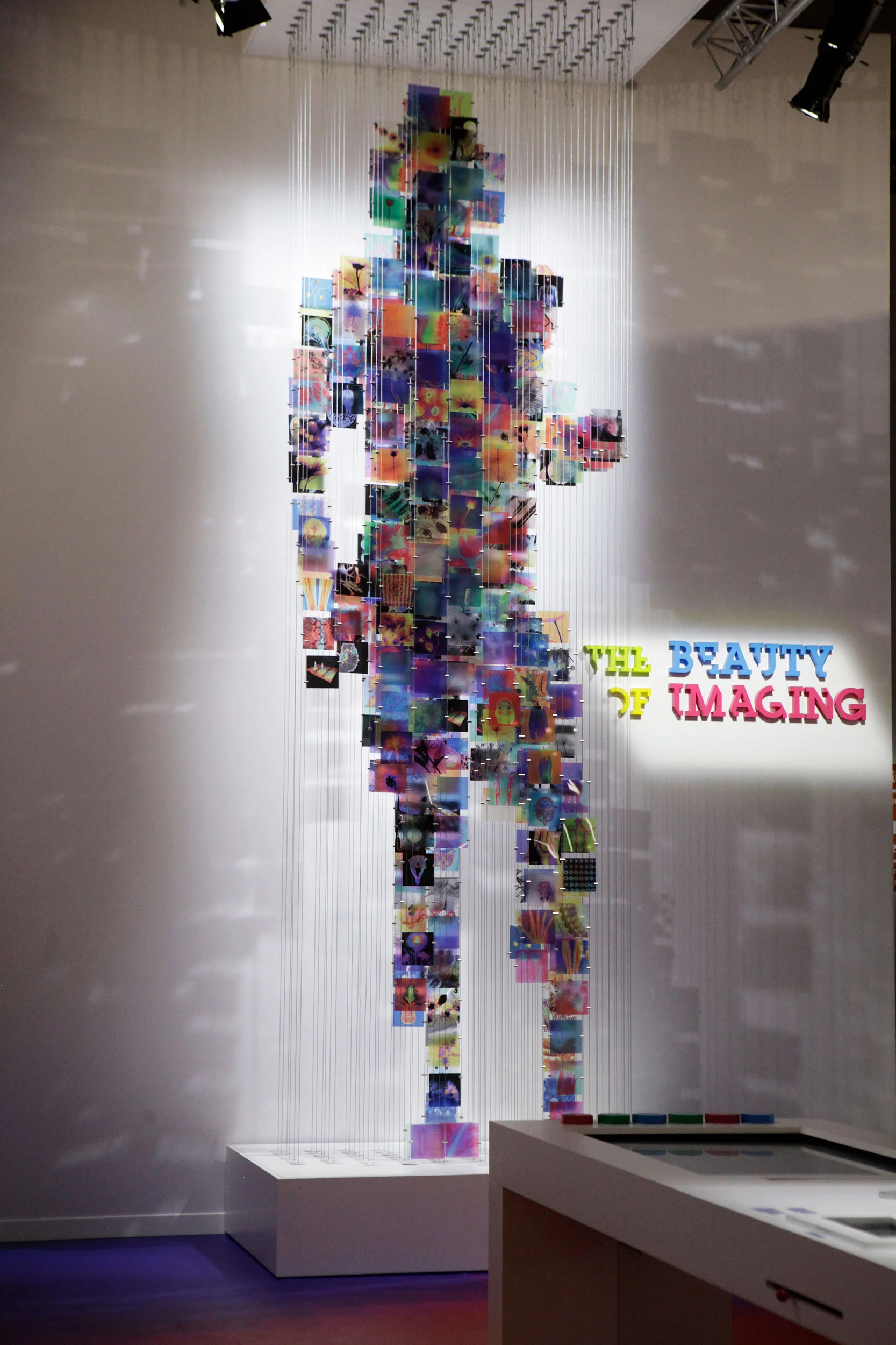Tall human silhouette made of hanging coloured medical images, next to The Beauty of Imaging title – Bracco The Beauty of Imaging, Milan, Italy, 2017 – exhibition design