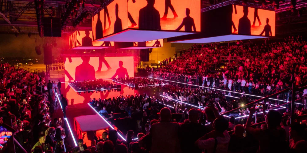 Hangar bathed in orange-red light, screens with black silhouettes of figures above the runways – Emporio Armani Boarding SS19, Milan, Italy, 2019 – fashion show set design