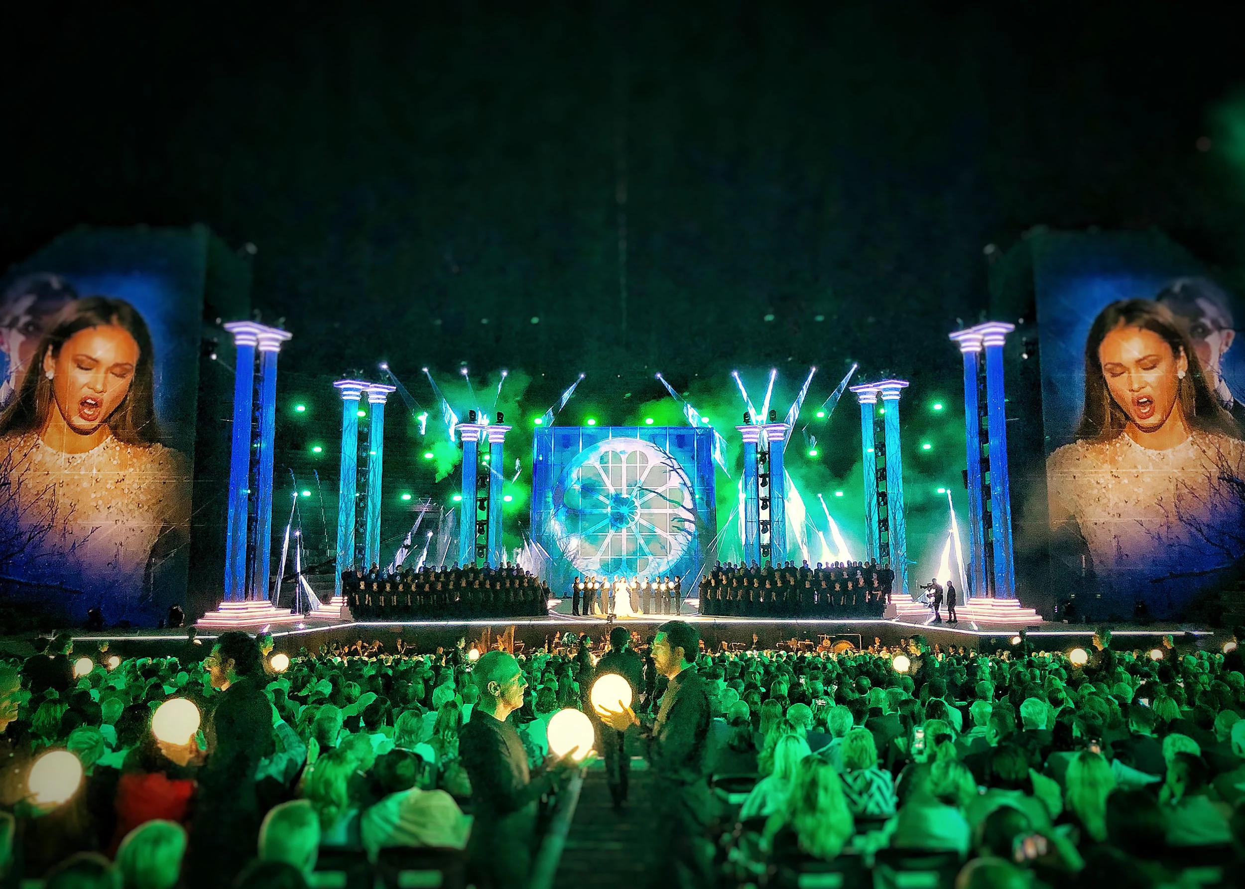 Stage in green light with a choir and a central rose-window panel, audience holding glowing spheres in the foreground – La Notte di Andrea Bocelli at the Arena di Verona, Italy, 2018 – concert stage design