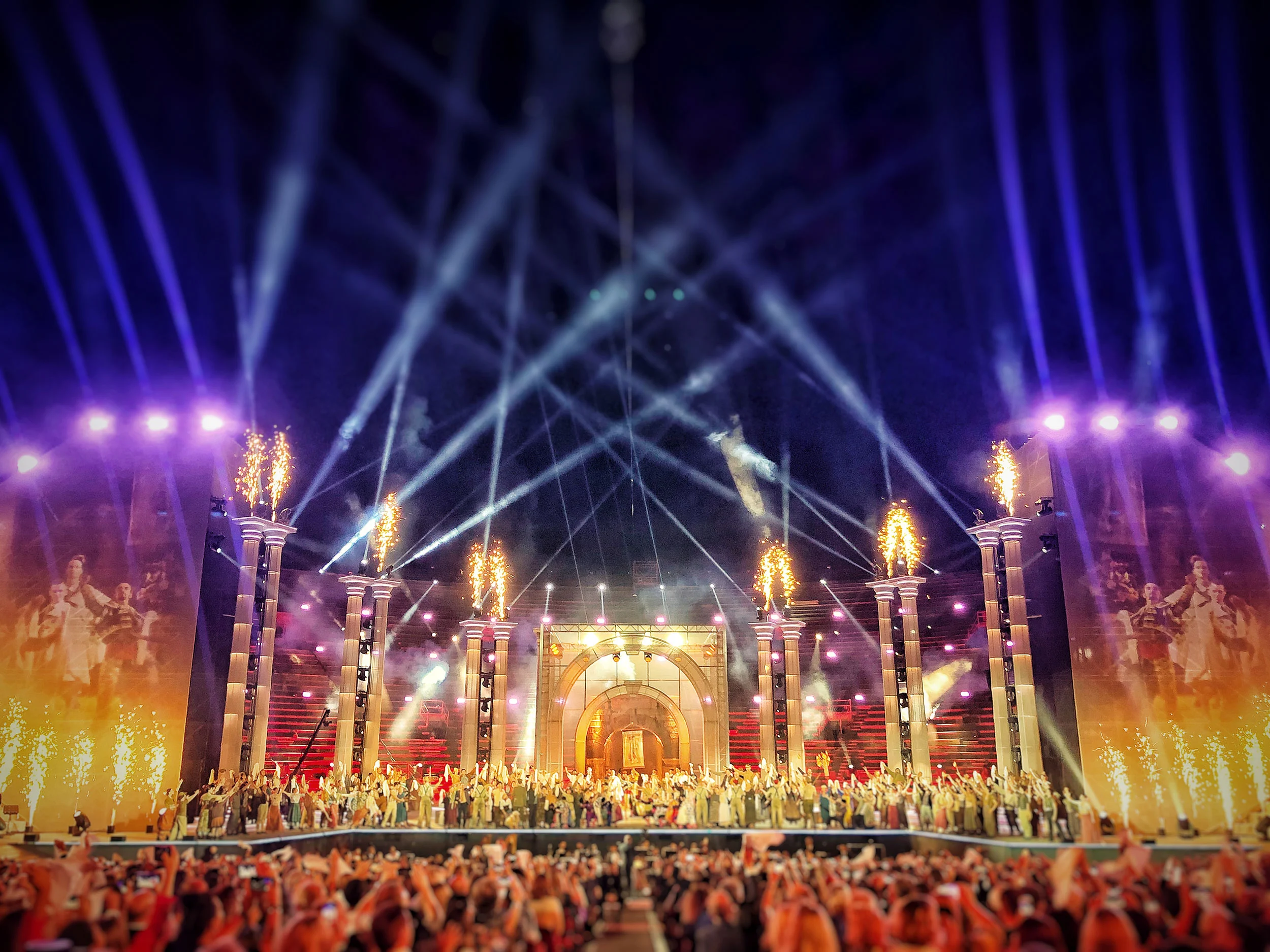 Arena di Verona stage for La Notte di Andrea Bocelli: flaming column tops, a central arch and the full cast under light beams – La Notte di Andrea Bocelli at the Arena di Verona, Italy, 2018 – concert stage design