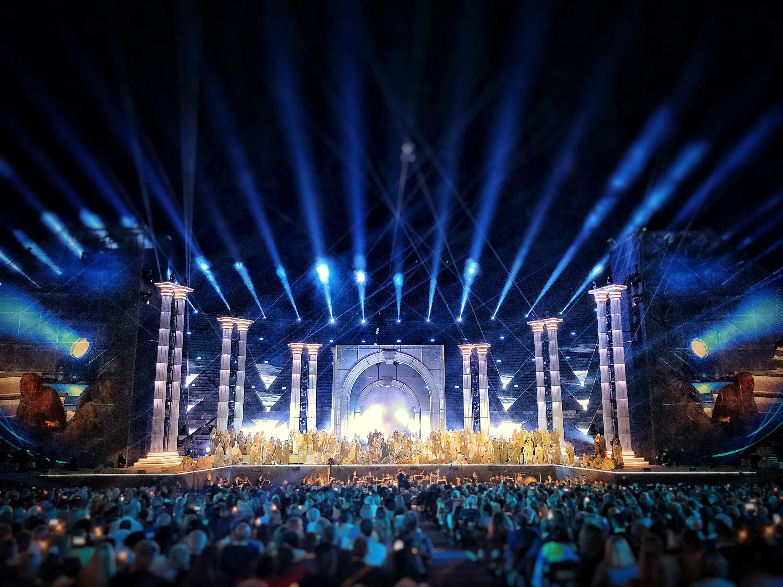 Blue light beams fanning out over the classical colonnade set, with the cast gathered under a bright central arch – La Notte di Andrea Bocelli at the Arena di Verona, Italy, 2018 – concert stage design