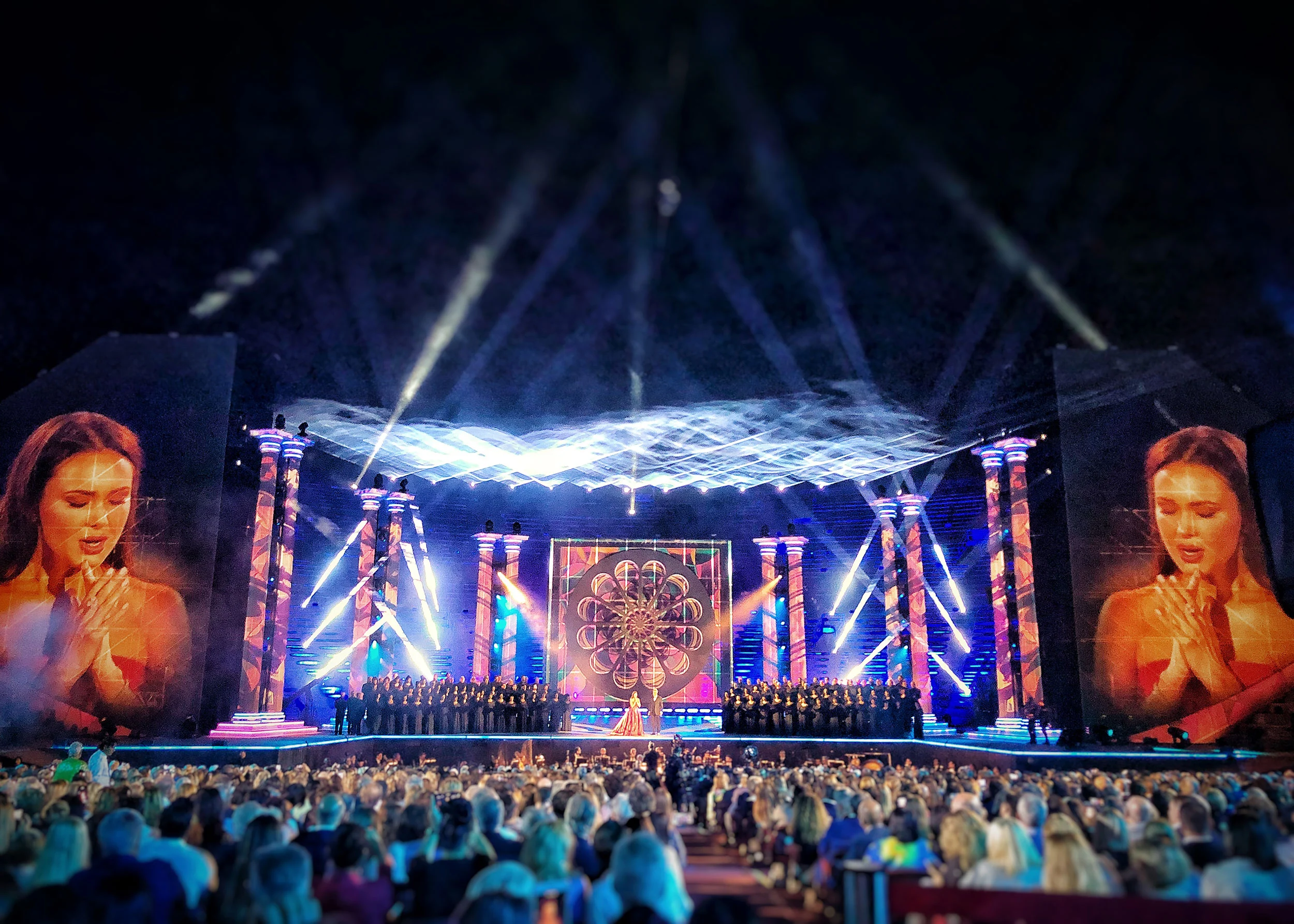 Choir on stage between striped columns, a rose-window panel at centre and a singer shown on the giant side screens – La Notte di Andrea Bocelli at the Arena di Verona, Italy, 2018 – concert stage design