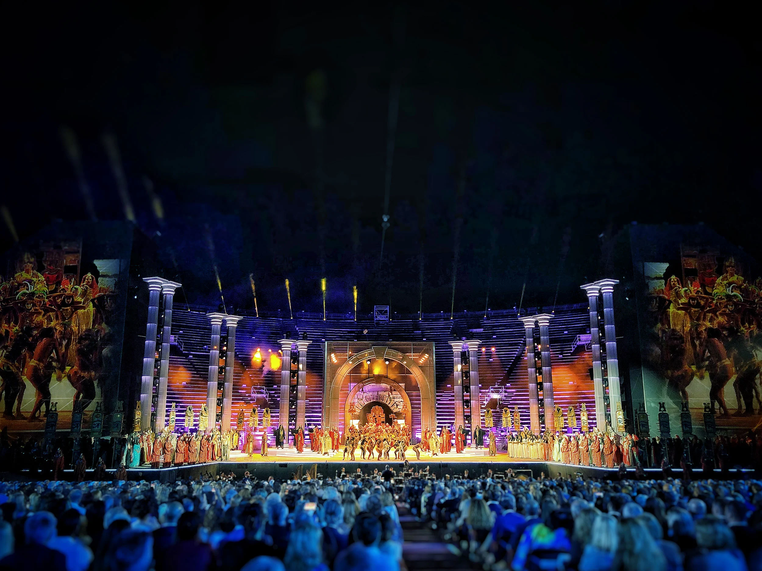 Night view of the Arena stage: columns, glowing central arch and a large costumed cast lined up before the audience – La Notte di Andrea Bocelli at the Arena di Verona, Italy, 2018 – concert stage design