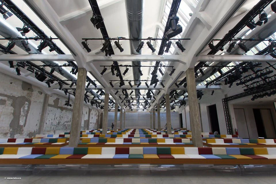 Fashion show venue with long benches in coloured stripes under rows of spotlights and white roof trusses – Marni Spring 2017 Ready-to-Wear, Milan, Italy – fashion show set design