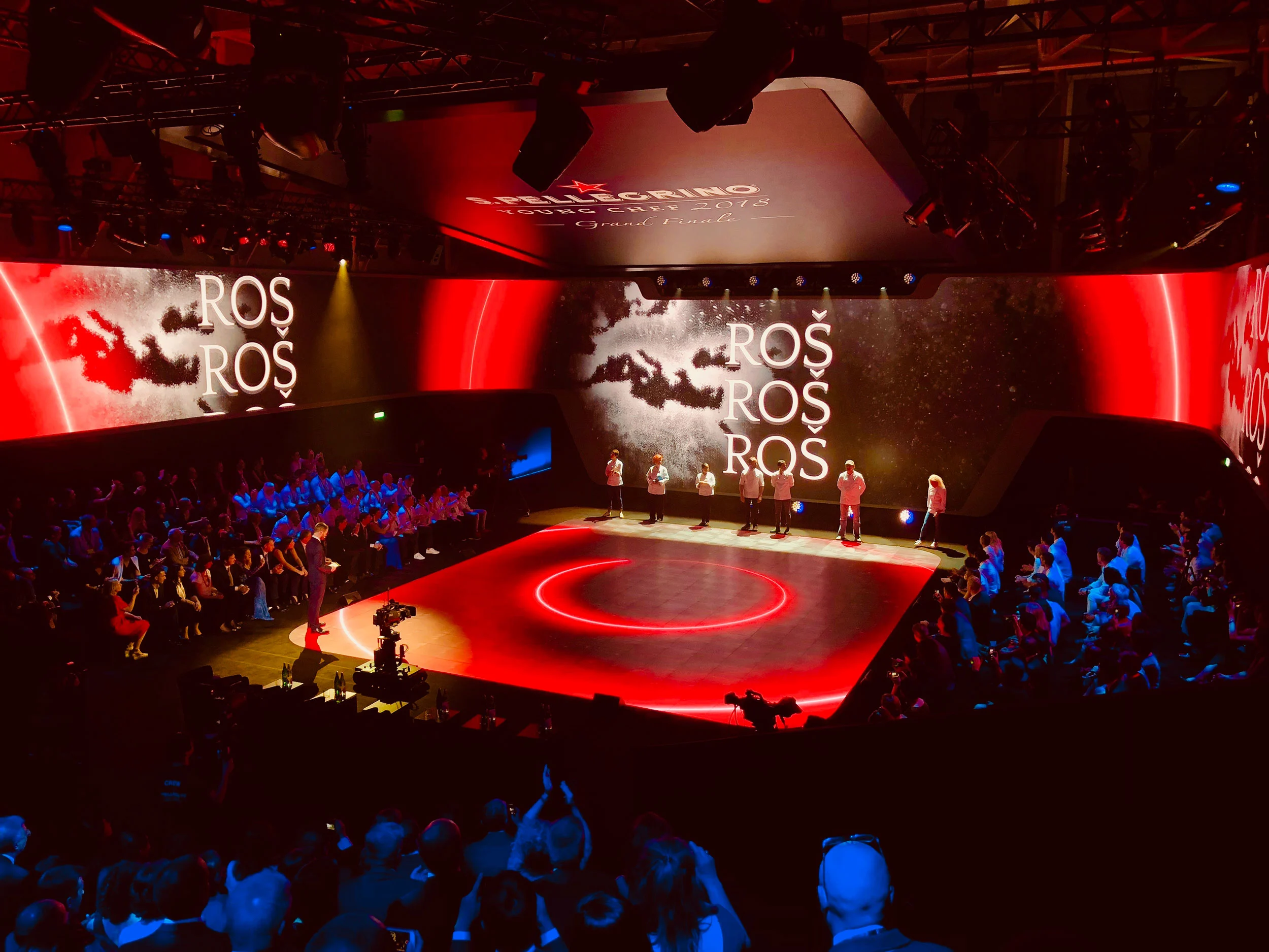 S.Pellegrino Young Chef final: chefs on a red-lit round stage before screens, audience around – S.Pellegrino Young Chef, Milan, Italy, 2019 – event design