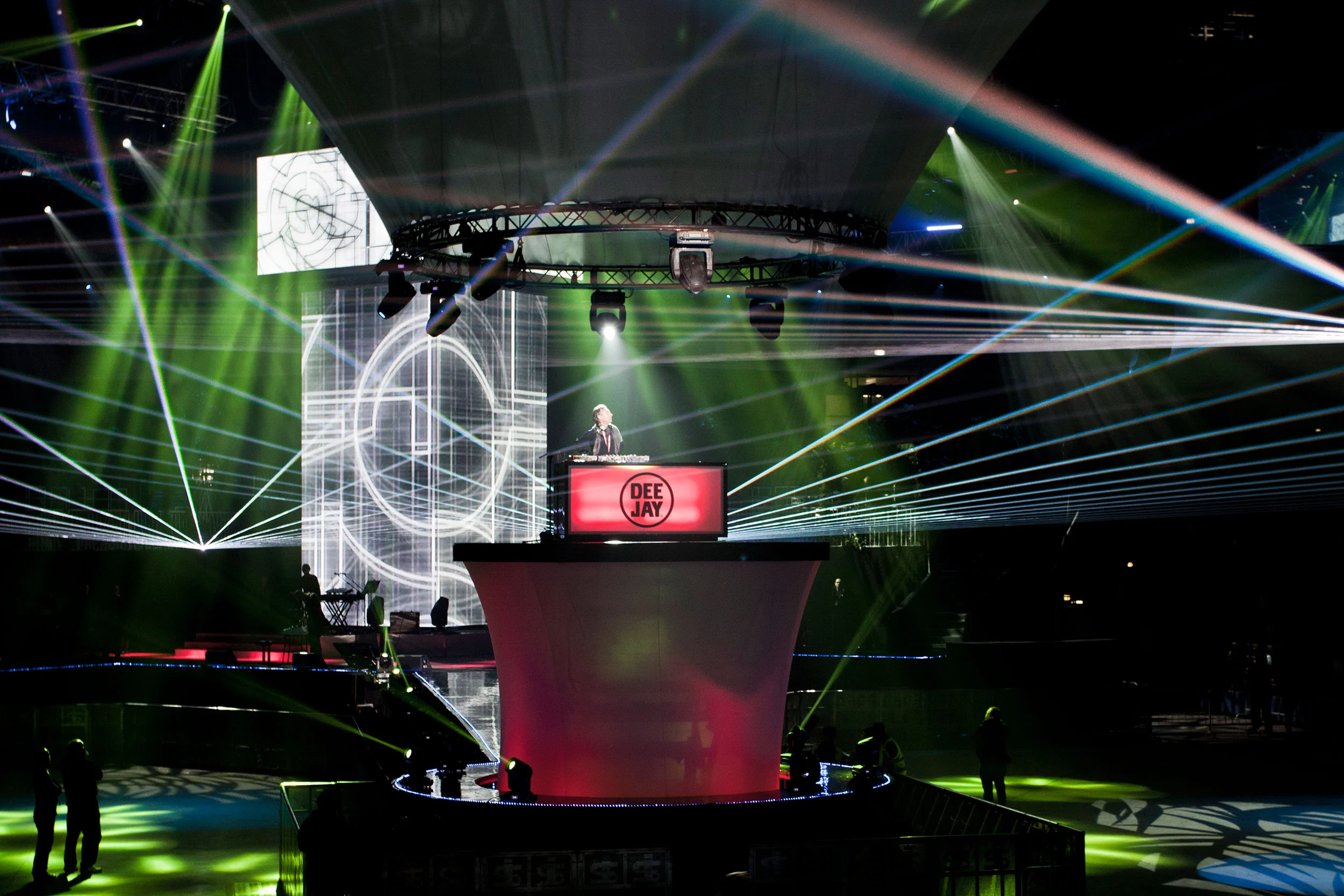 DJ console with a Deejay sign on a red round podium, crossed by green laser beams – Radio Deejay 30th Anniversary Party, Assago, Italy, 2019 – concert stage design