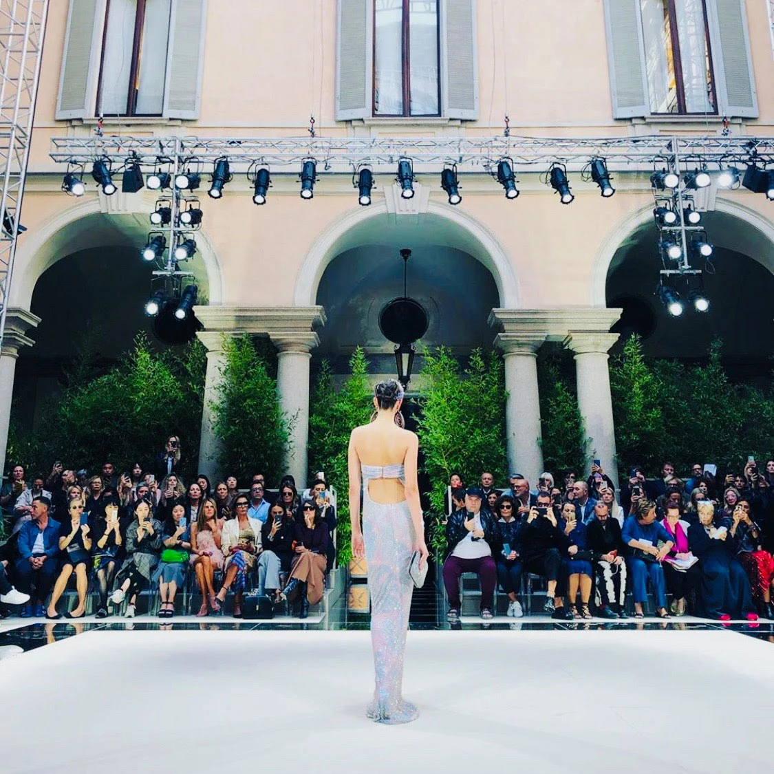 Model on the white runway seen from behind, facing guests seated under the arcade and a lighting rig – Giorgio Armani SS20 Men and Women, Milan, Italy, 2019 – fashion show set design
