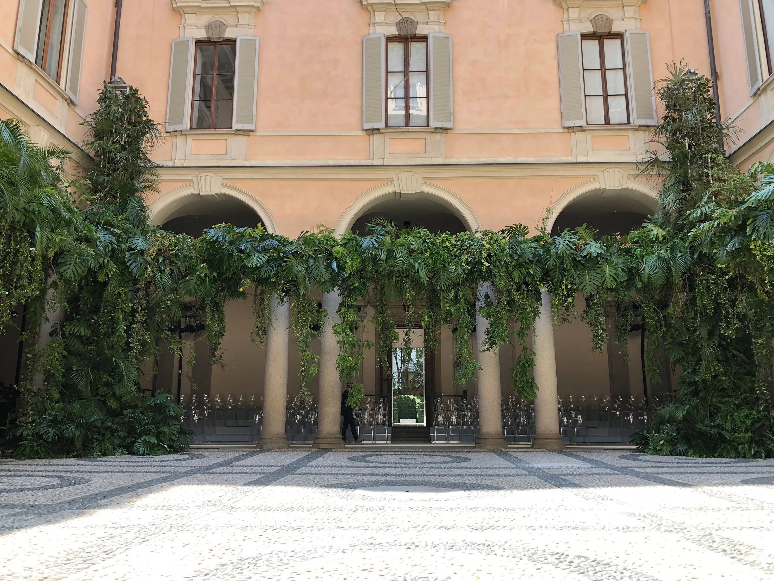 Palazzo Orsini courtyard with tropical plants spilling over the colonnade and cobbled floor – Giorgio Armani SS20 Men and Women, Milan, Italy, 2019 – fashion show set design