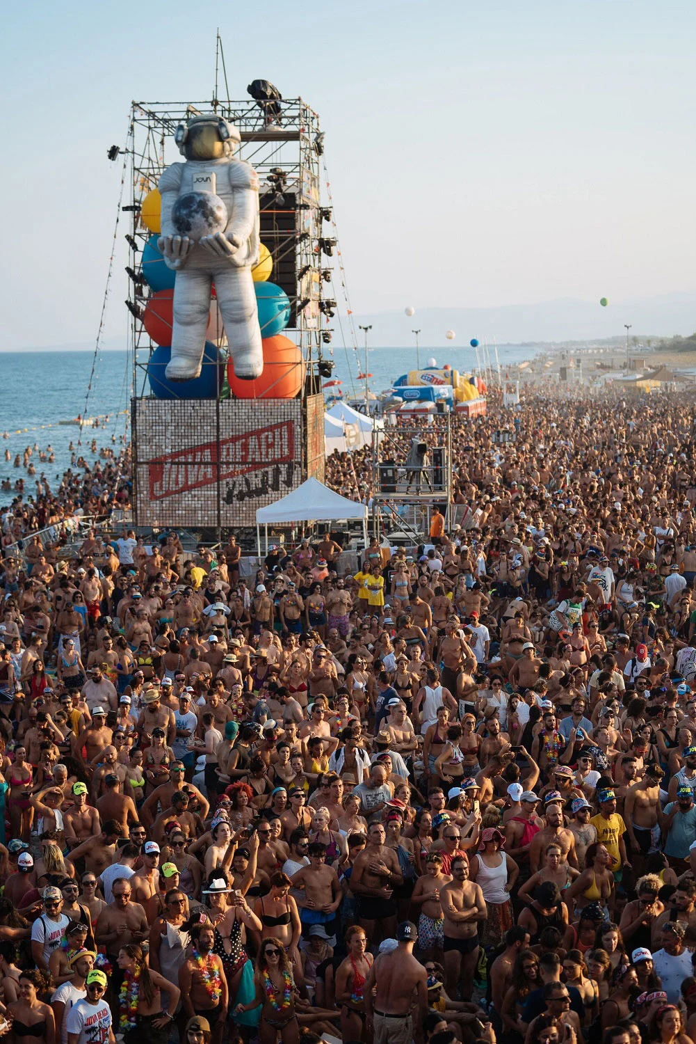 Giant inflatable astronaut on a scaffold tower above a crowd stretching along the beach to the sea – Jova Beach Party 2019, Italy – concert stage design