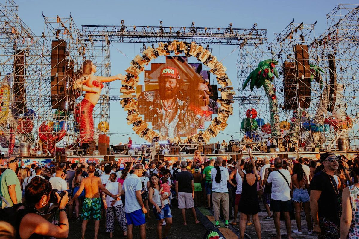 Crowd in the afternoon sun before the stage, with a mermaid figure and palm trees on the scaffold towers – Jova Beach Party 2019, Italy – concert stage design