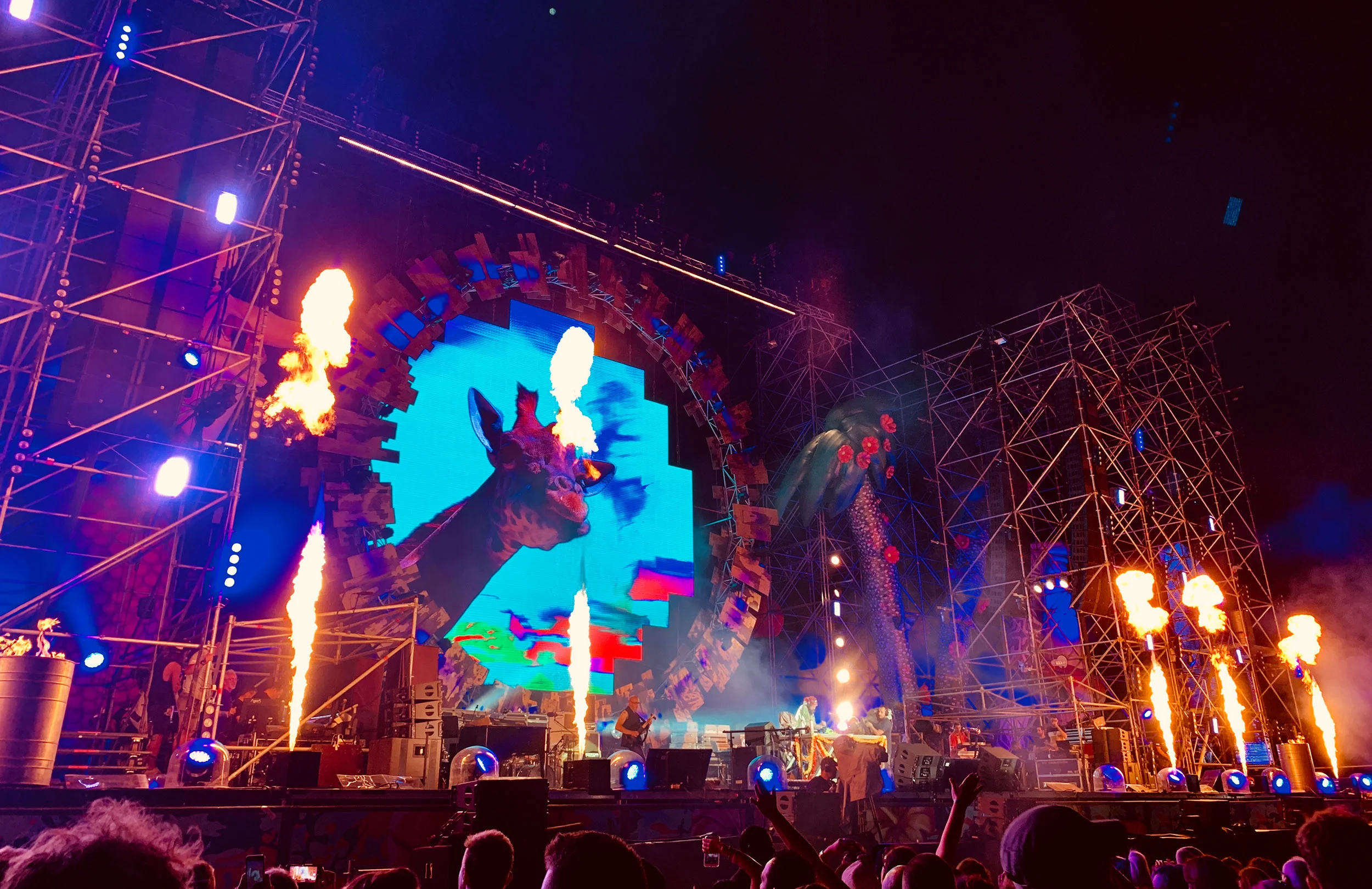 Night show with flame jets firing in front of the ring screen and blue-lit scaffold towers – Jova Beach Party 2019, Italy – concert stage design