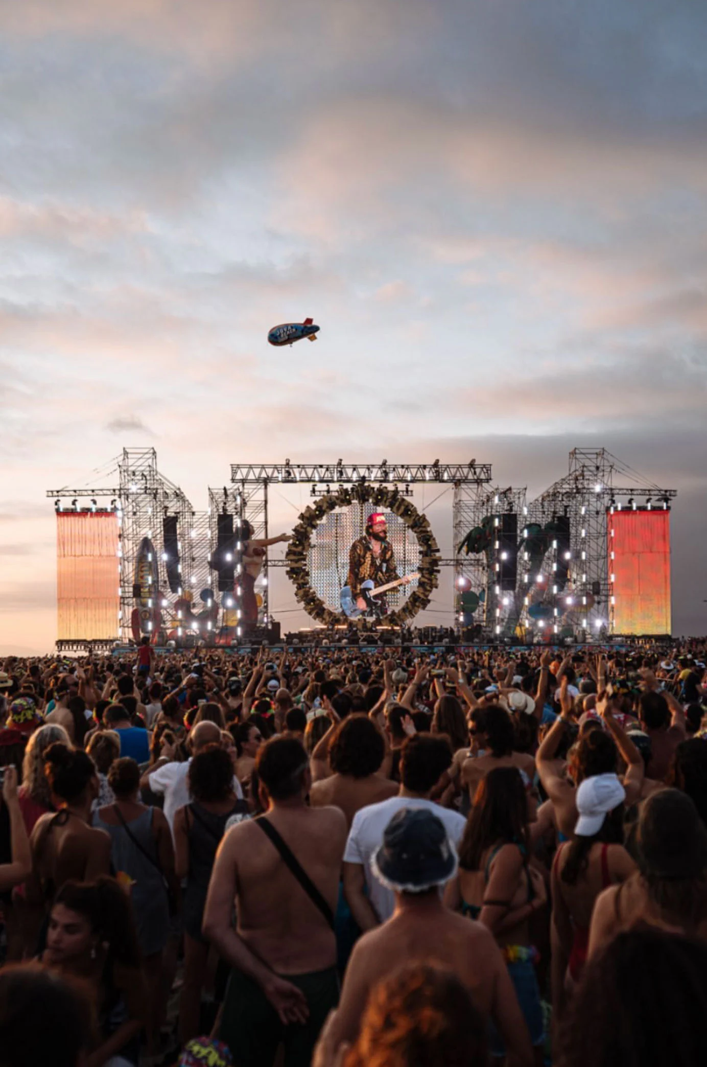 Crowd at sunset before the Jova Beach stage, with a blimp flying above the scaffolding – Jova Beach Party 2019, Italy – concert stage design