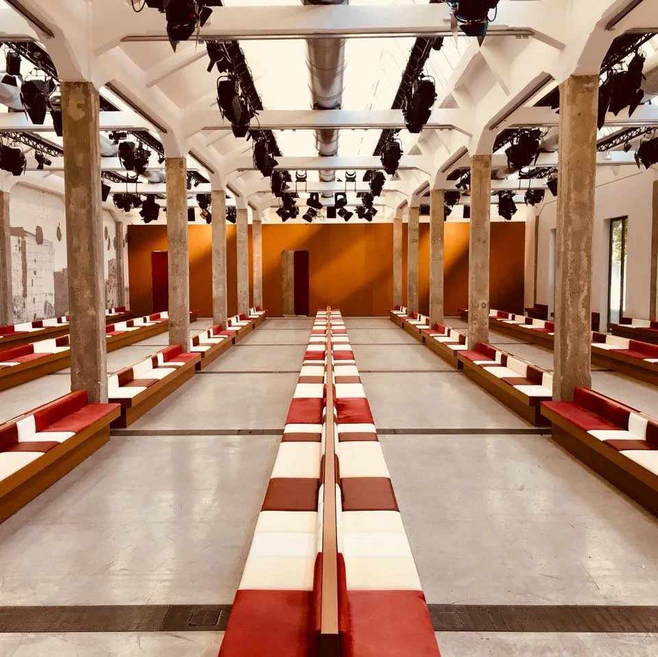 Marni AW 2017 venue: long red and white benches between concrete pillars, an orange wall at the end – Marni AW 2017, Milan, Italy – fashion show set design