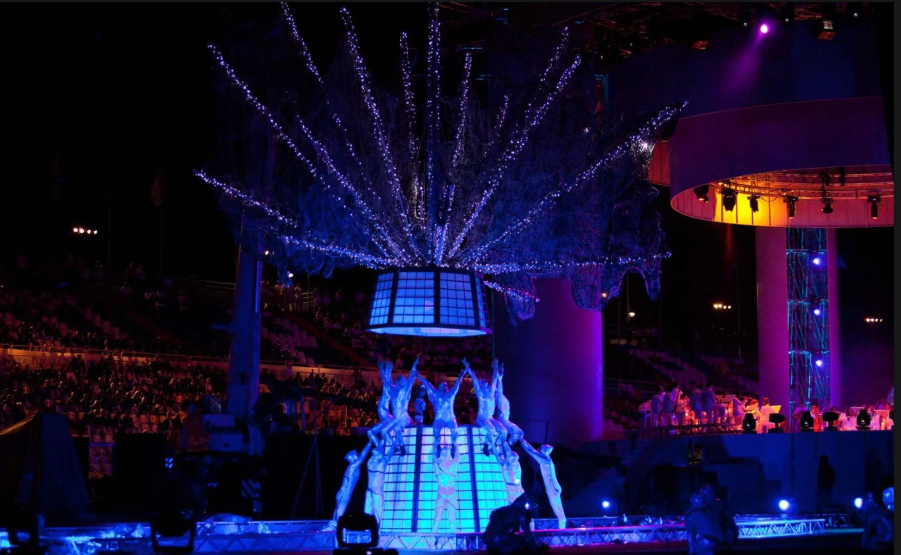 Acrobats in white posing below a glowing lantern crowned with branches of white lights – Pescara 2009 Mediterranean Games Opening Ceremony, Italy, 2019 – event design