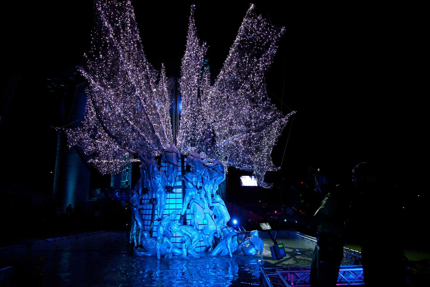 Sculpted tree of tangled figures with branches of white lights, lit blue at night – Pescara 2009 Mediterranean Games Opening Ceremony, Italy, 2019 – event design
