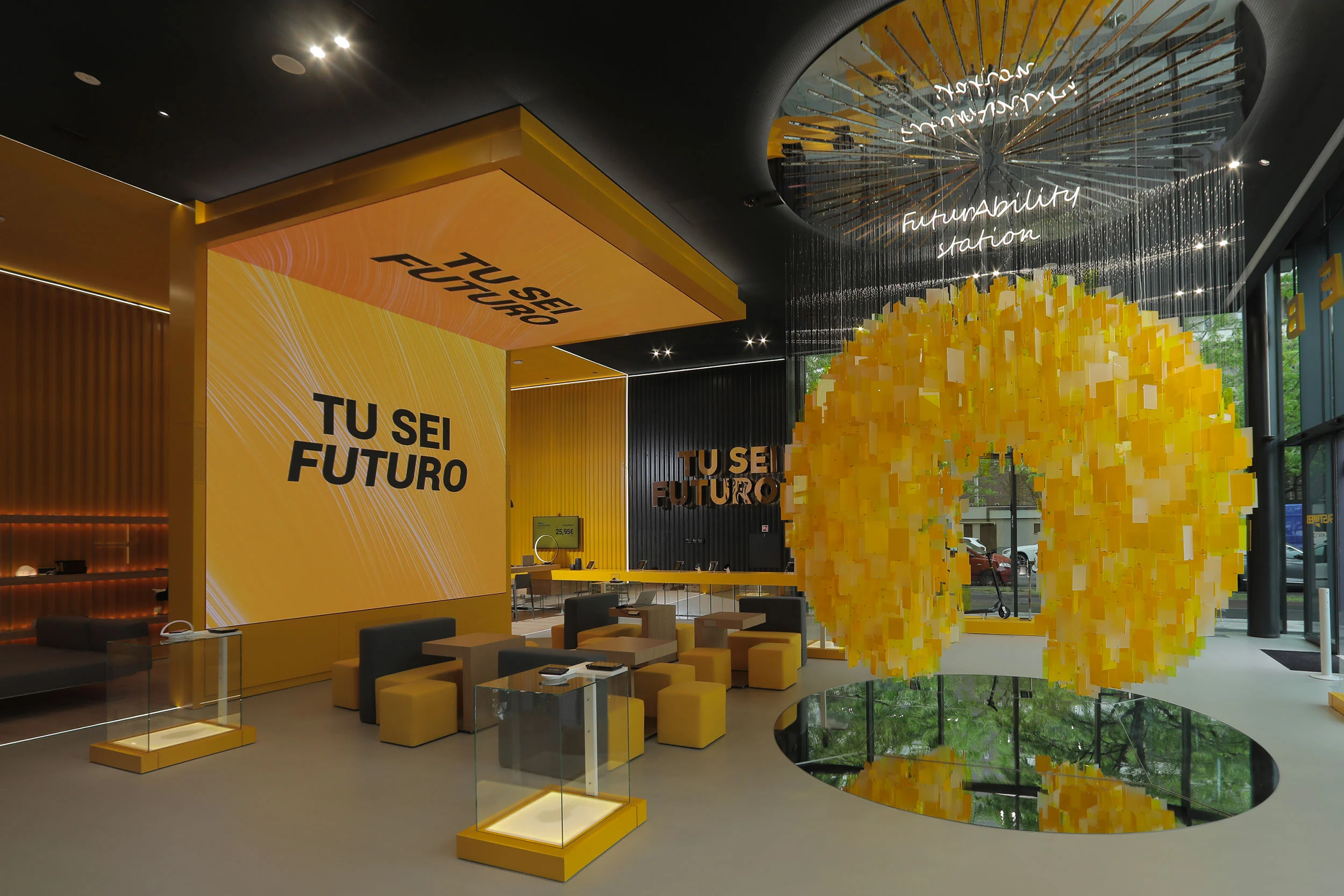 Entrance hall with yellow "Tu sei futuro" screens, lounge seating and a suspended sphere of yellow tiles over a mirror – STEP FuturAbility District by Fastweb, Milan, Italy, 2022 – exhibition design
