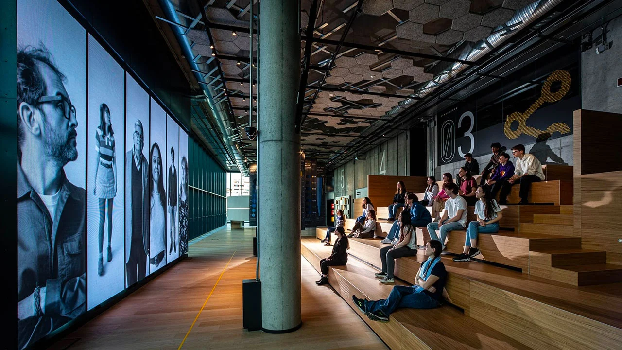 Young visitors on wooden tiered seating facing a wall of large black-and-white portrait screens – STEP FuturAbility District by Fastweb, Milan, Italy, 2022 – exhibition design