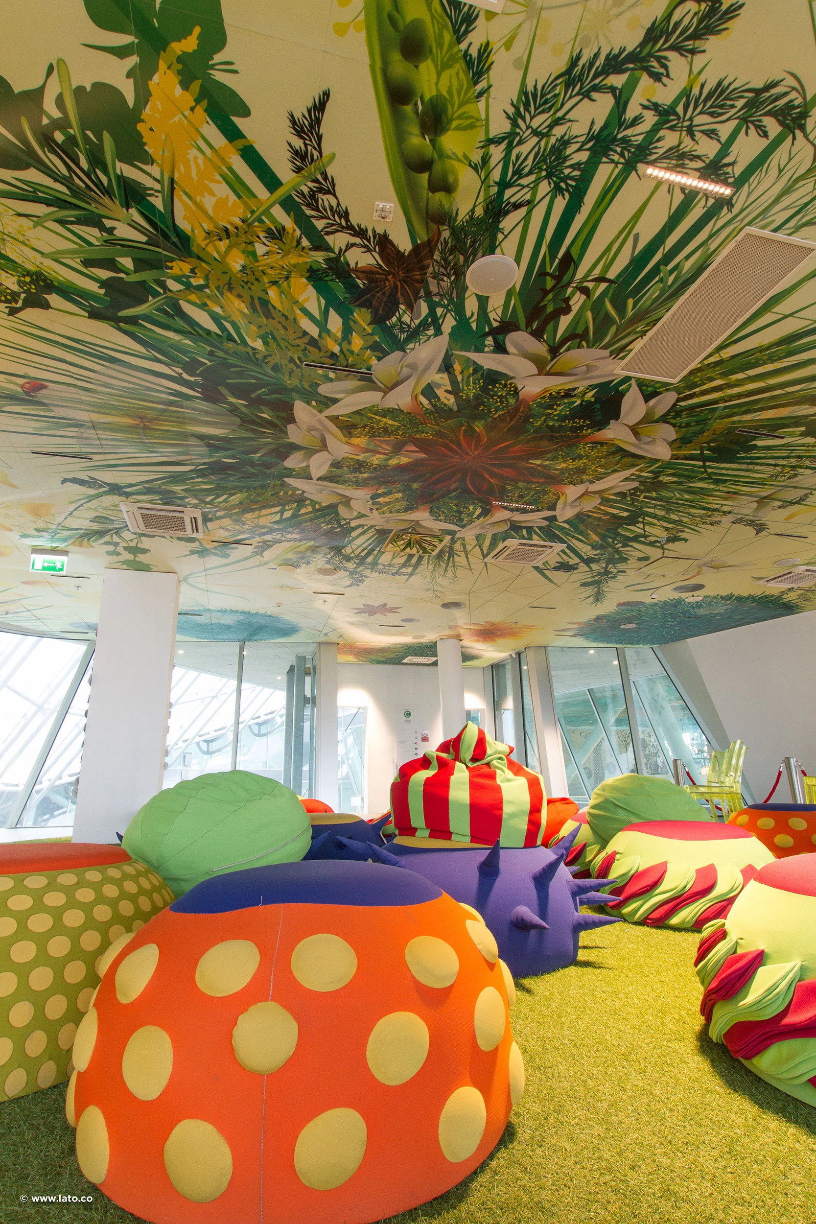 Playroom with a giant painted plant canopy on the ceiling and fruit-shaped soft seats on green carpet – Italian Pavilion at Expo 2015, Milan, Italy – exhibition design