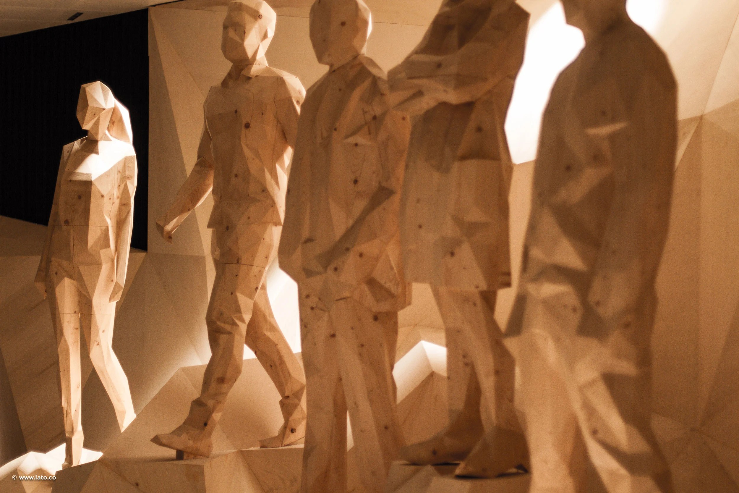Faceted wooden figures of people walking across a sculpted timber landscape, lit warm from the side – Italian Pavilion at Expo 2015, Milan, Italy – exhibition design