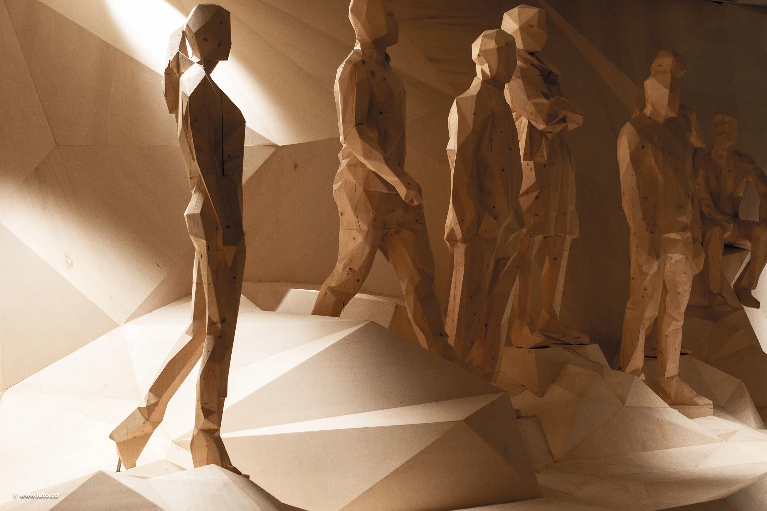 Row of faceted wooden human sculptures striding over angular plywood terrain in raking light – Italian Pavilion at Expo 2015, Milan, Italy – exhibition design