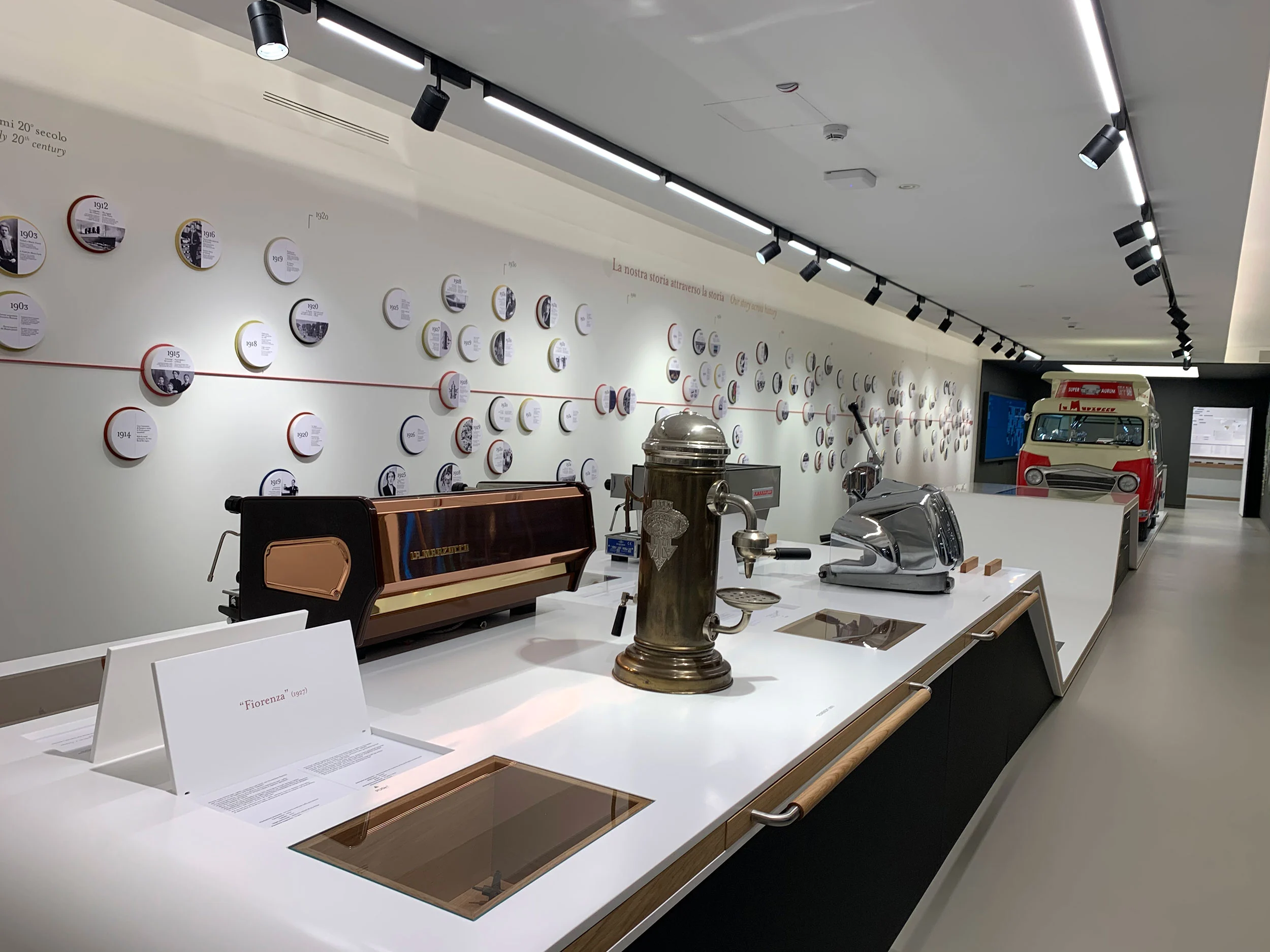 Museum counter displaying historic espresso machines, a timeline of round photos and a vintage van – La Marzocco Accademia del Caffè Espresso, Florence, Italy, 2018 – interior design