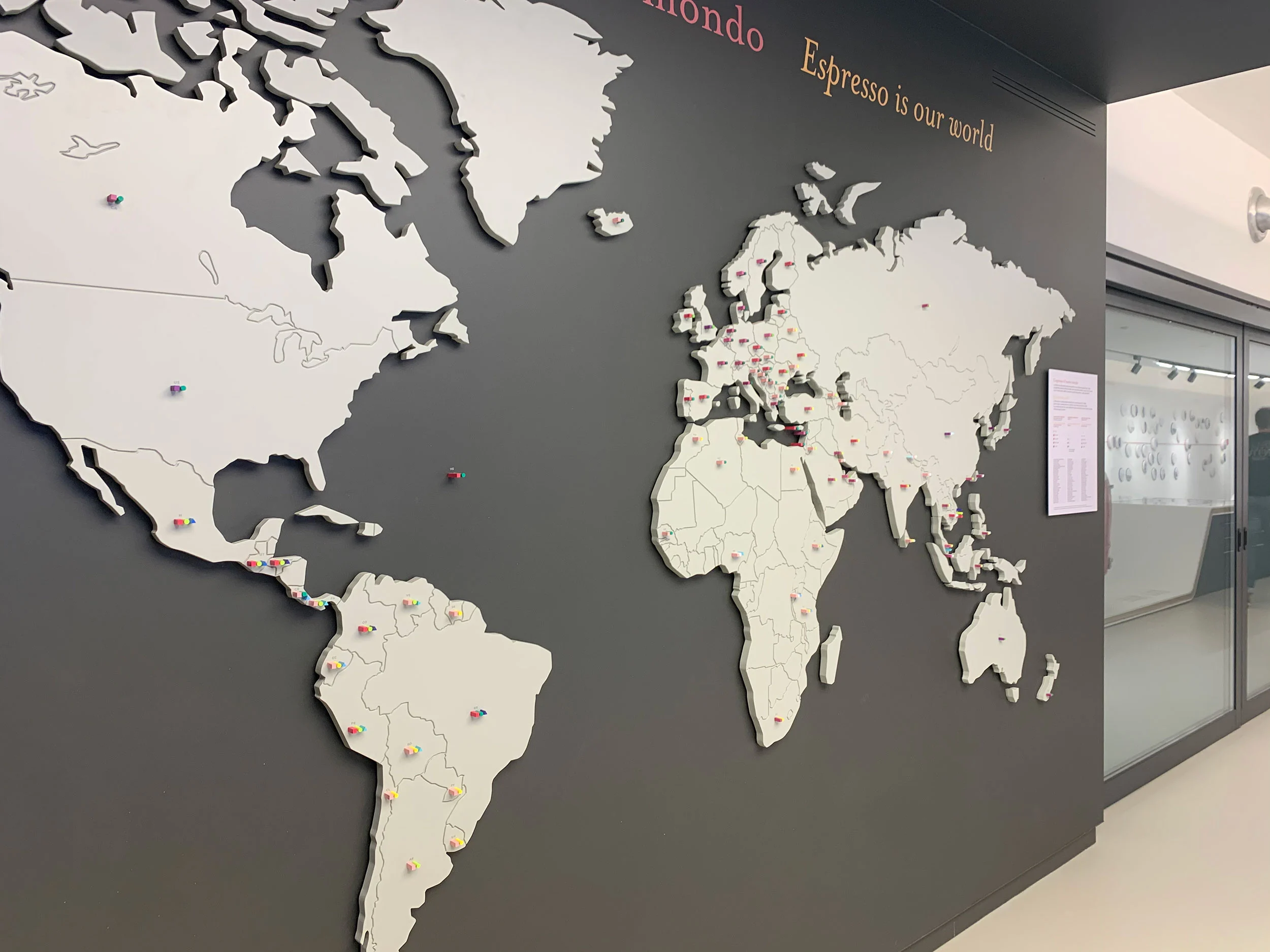 Wall-sized world map with raised white continents and the words Espresso is our world – La Marzocco Accademia del Caffè Espresso, Florence, Italy, 2018 – interior design
