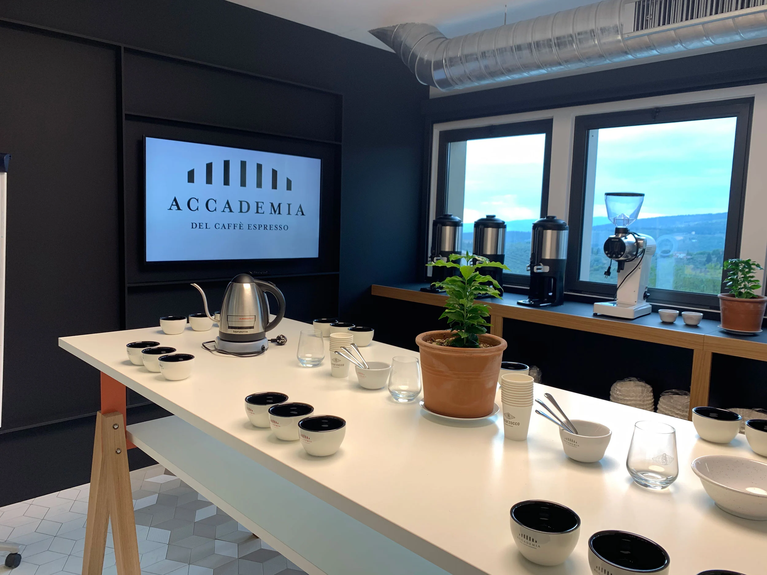 Training room with a long white table set for coffee cupping, grinders by windows on the hills – La Marzocco Accademia del Caffè Espresso, Florence, Italy, 2018 – interior design