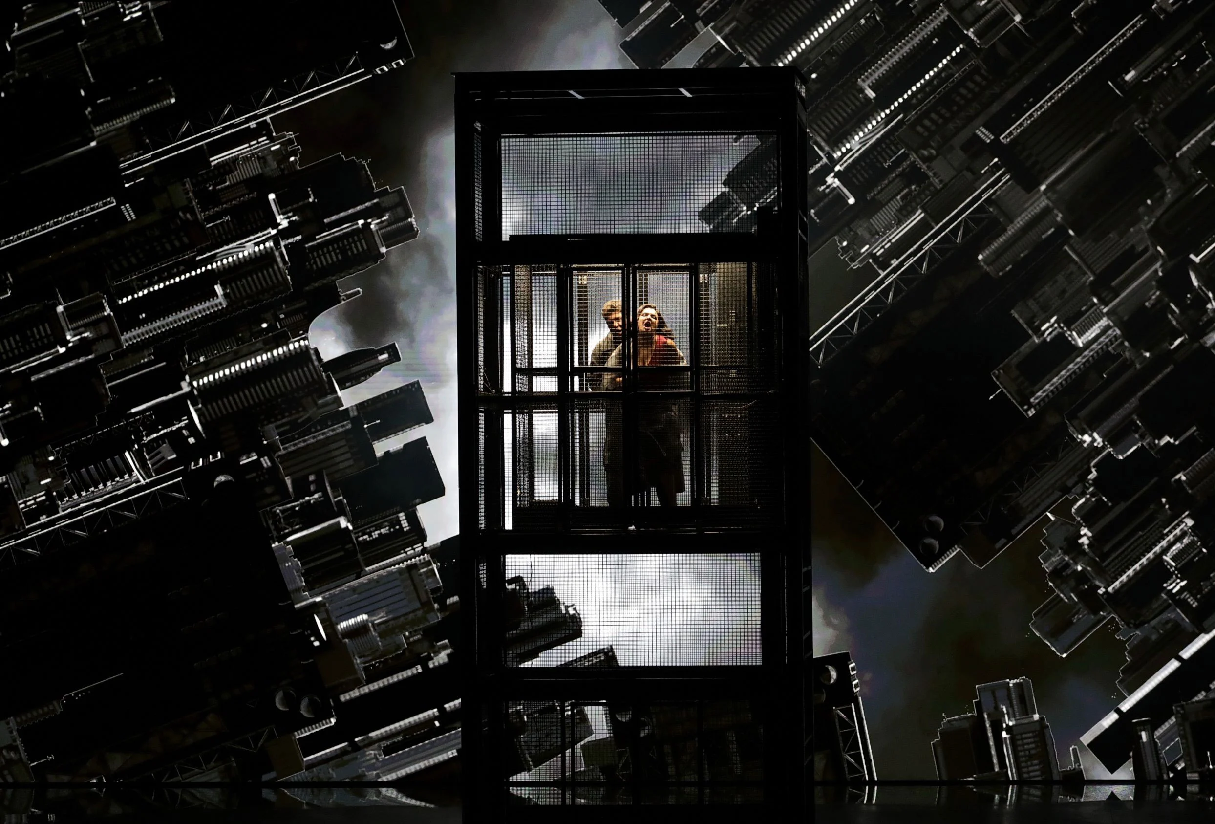 Two singers in a glass elevator cage among projections of overturned skyscrapers – Macbeth at La Scala, Milan, Italy, 2021 – opera set design